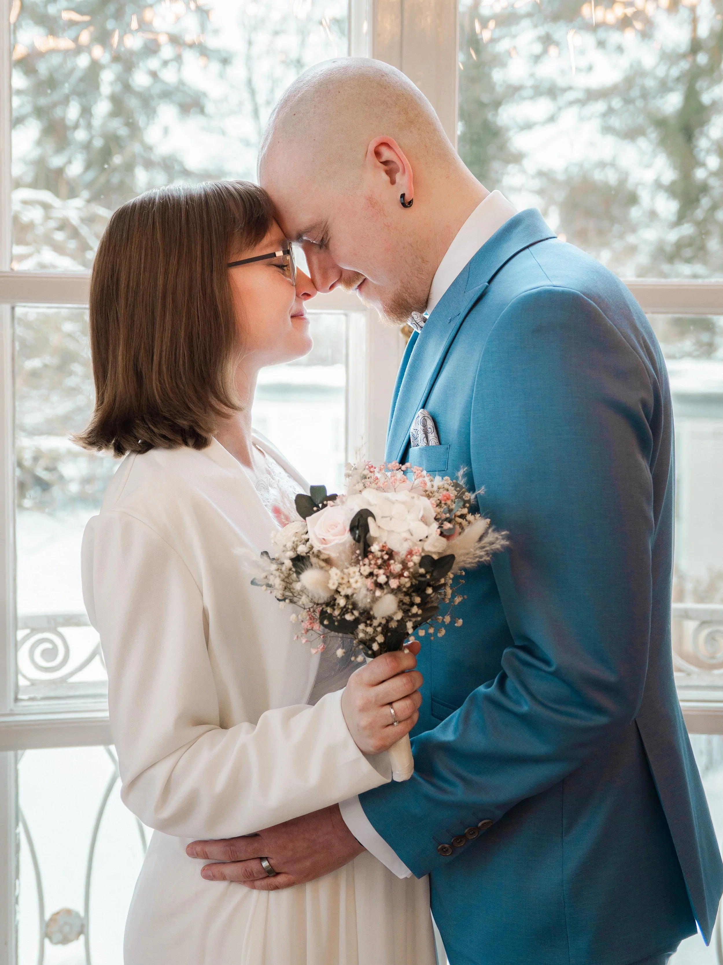 Ein Brautpaar lehnt im Schnee vor dem Standesamt Lübeck Kopf an Kopf. Im Hintergrund sind die verschneiten Bäume zu sehen.