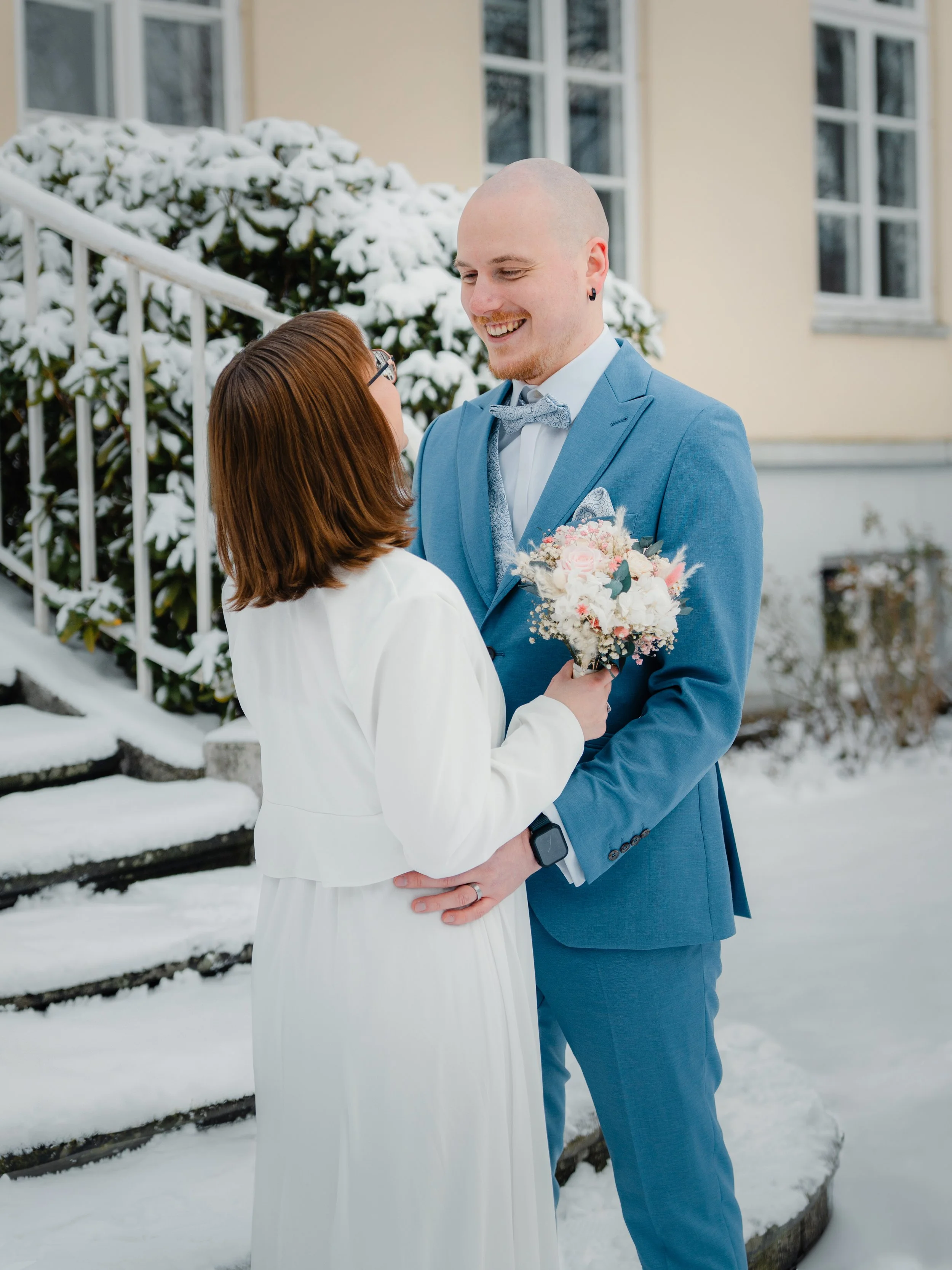 Standesamtliche Trauung in Lübeck im Winter  das Brautpaar steht eng zusammen im Schnee, während im Hintergrund die verschneiten Bäume den Moment einrahmen.