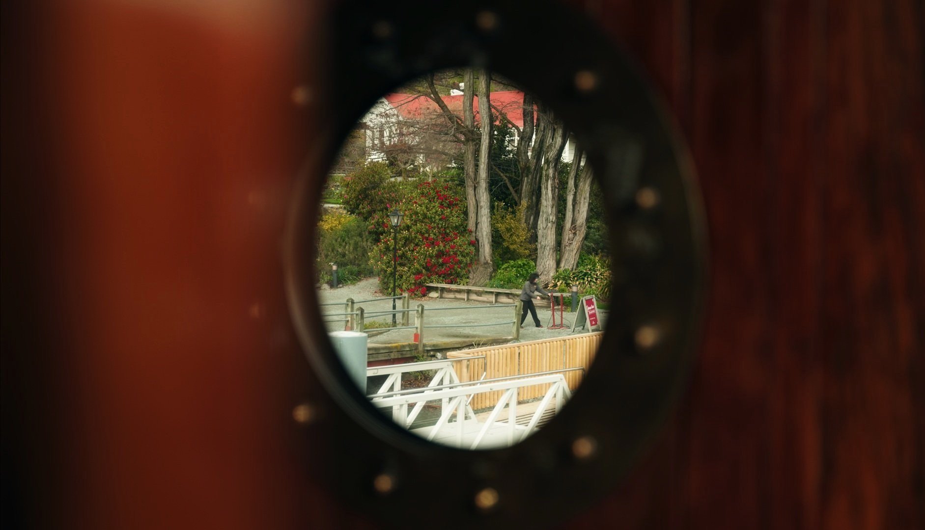 View of a park through the sound hole of a guitar showing trees, bushes, a person walking, and park signage.