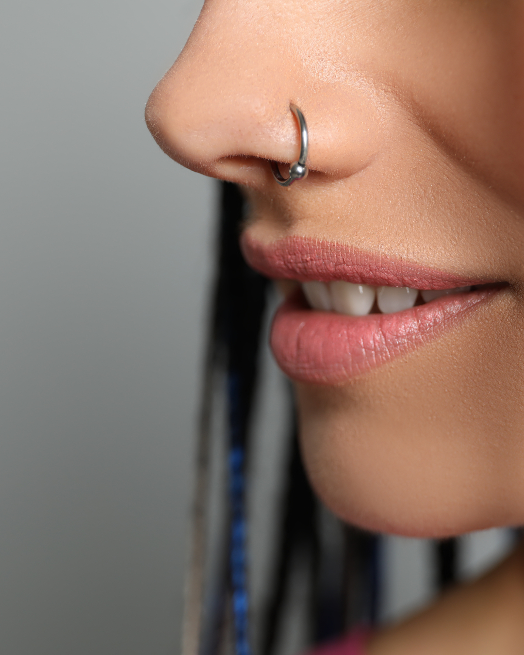 Close-up of a woman's face showing her nose with a septum piercing and her lips slightly parted, revealing teeth.