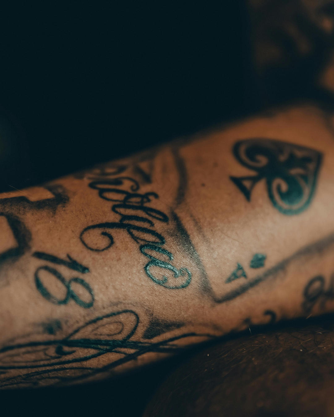 Close-up of tattooed skin with various black ink tattoos, including script writing, star shapes, and decorative designs.