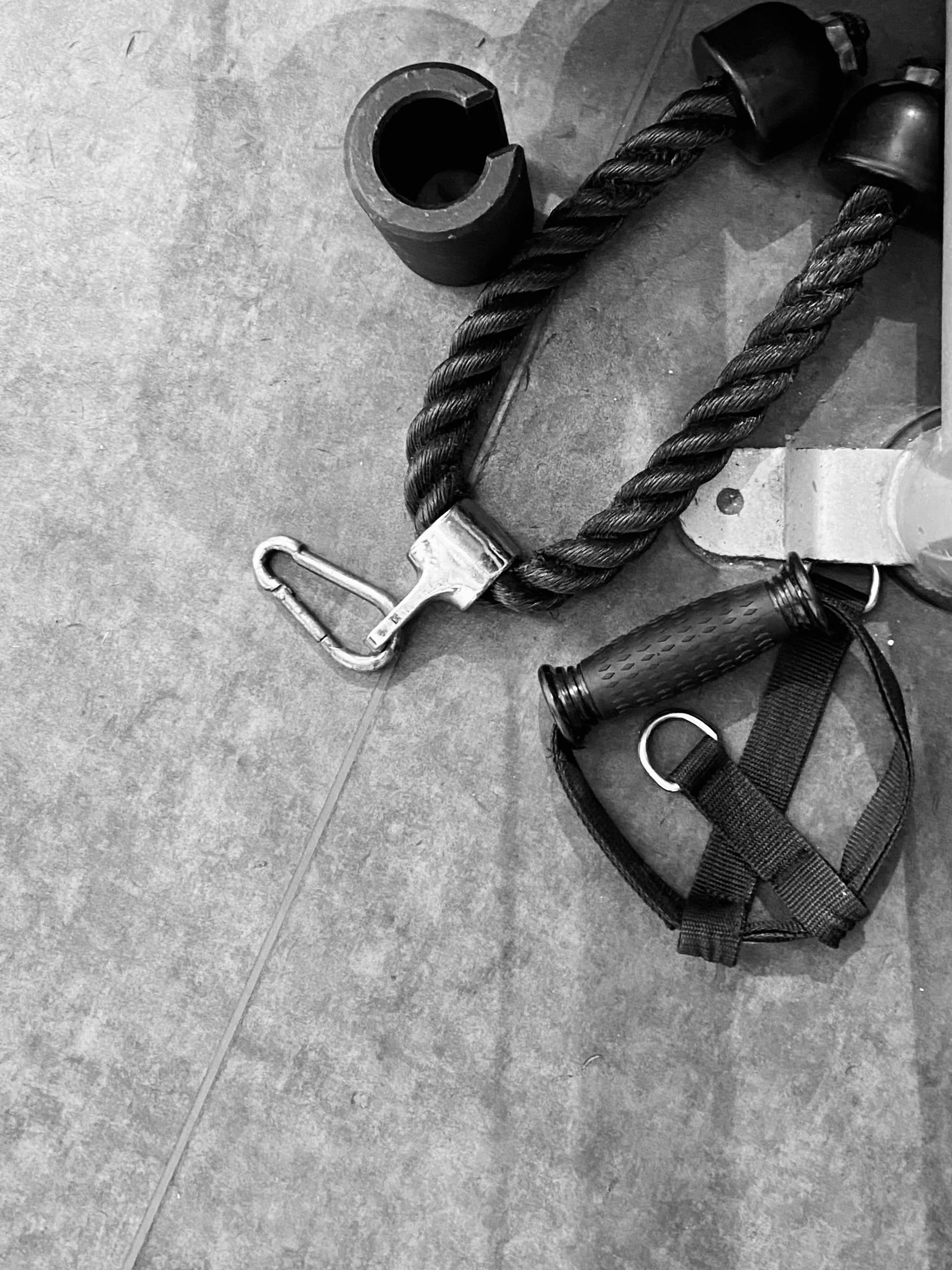 Workout equipment including a resistance band, a rope with a carabiner, and a foam roller placed on a tiled floor.