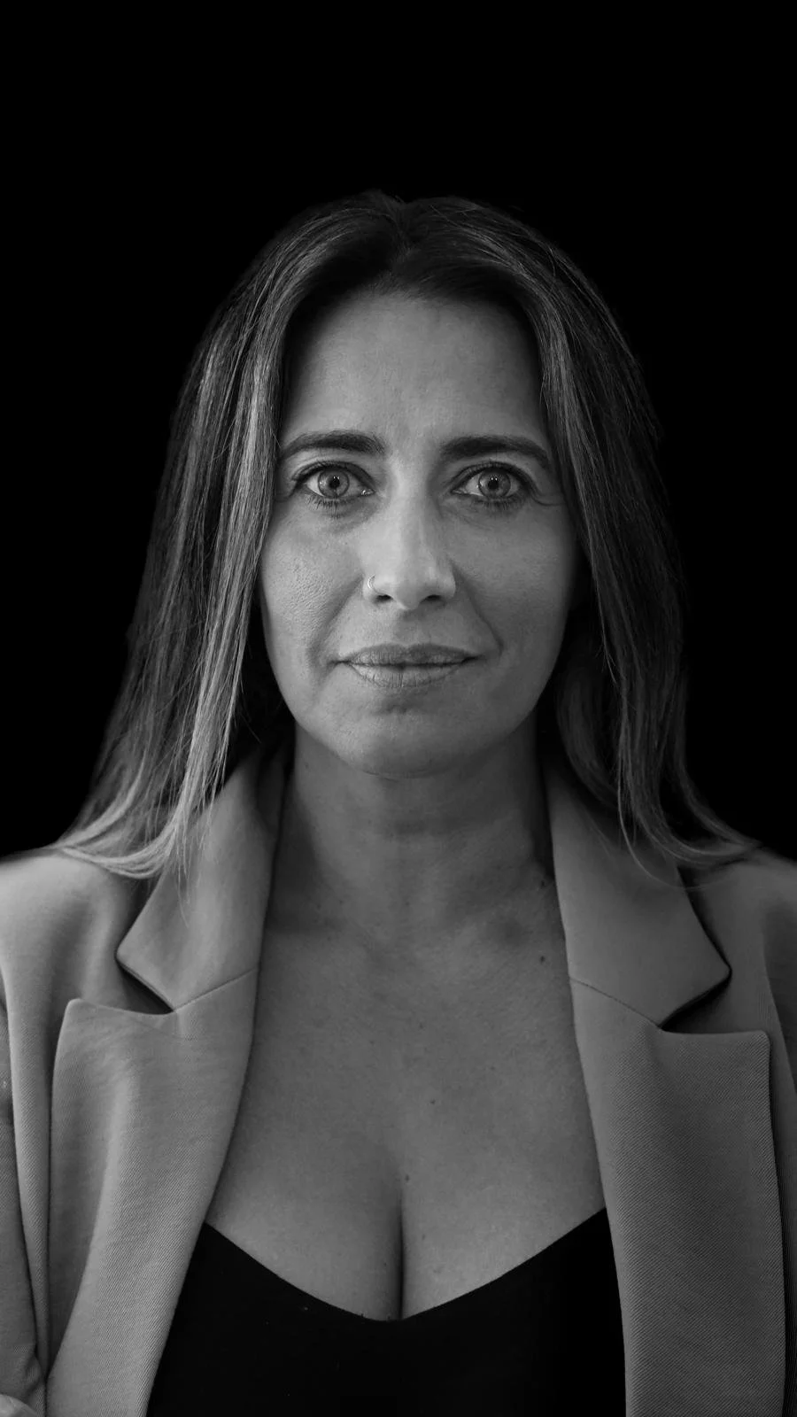 Retrato em preto e branco de uma mulher com cabelo médio, olhos claros, usando uma blusa escura e uma blusa clara por cima, com um fundo preto.