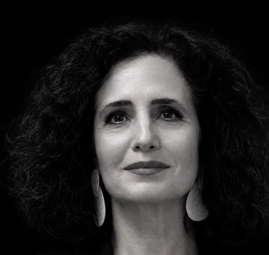 Retrato de uma mulher com cabelo cacheado, vestindo jaqueta com riscas e brincos grandes