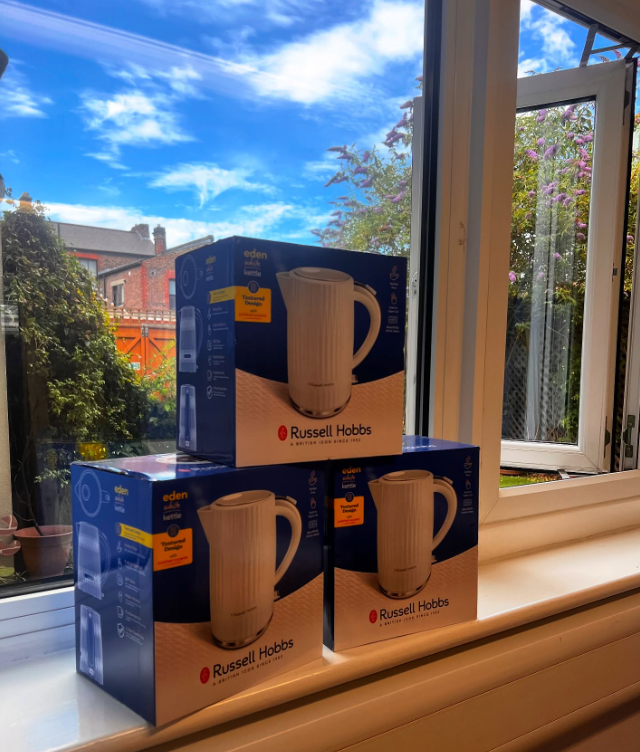 Three boxes of Russell Hobbs electric kettle placed on a windowsill in front of a sunny window with a view of trees and houses outside.
