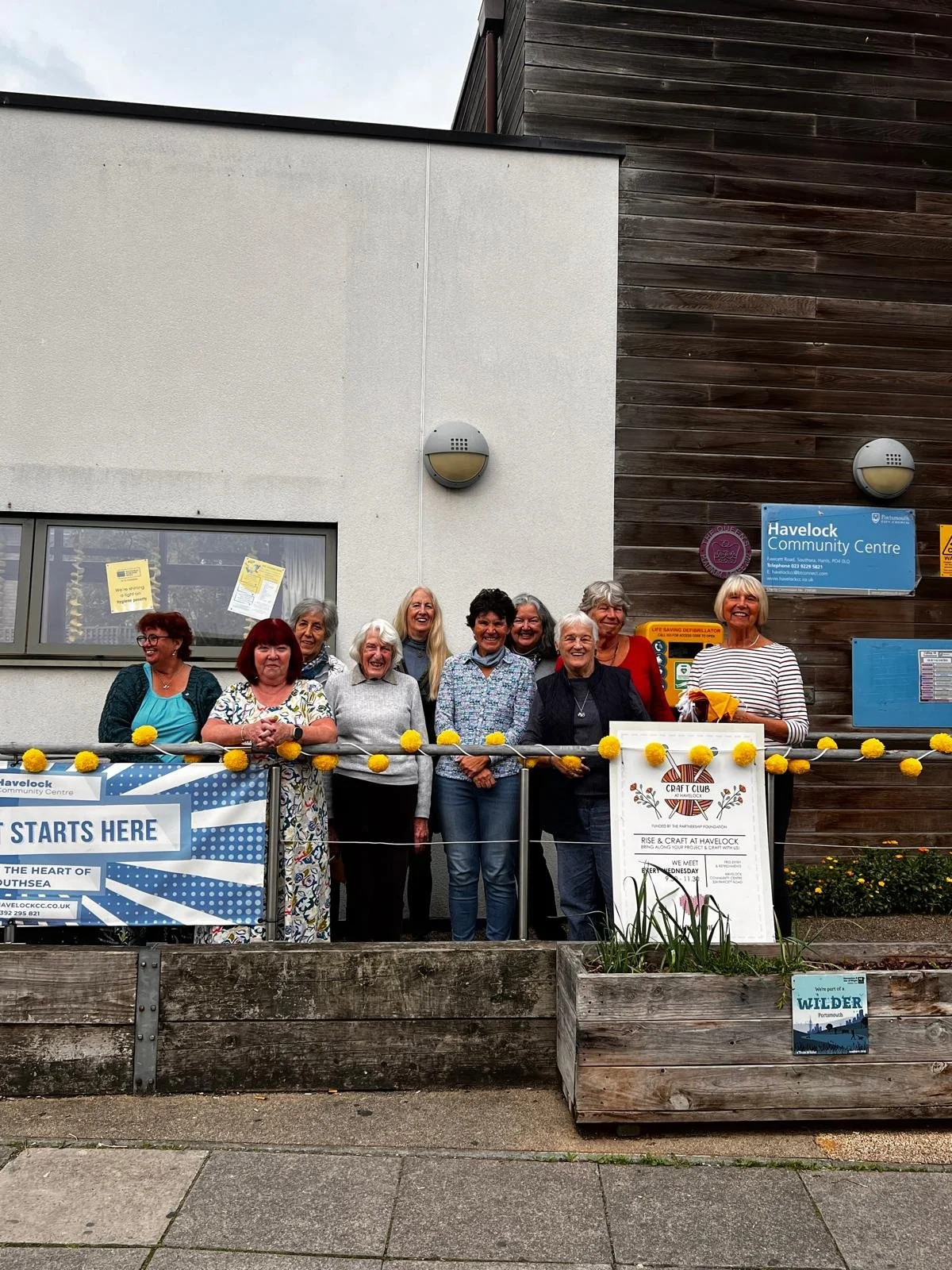 Group of women standing on a patio in front of a building with signs, smiling for the camera.