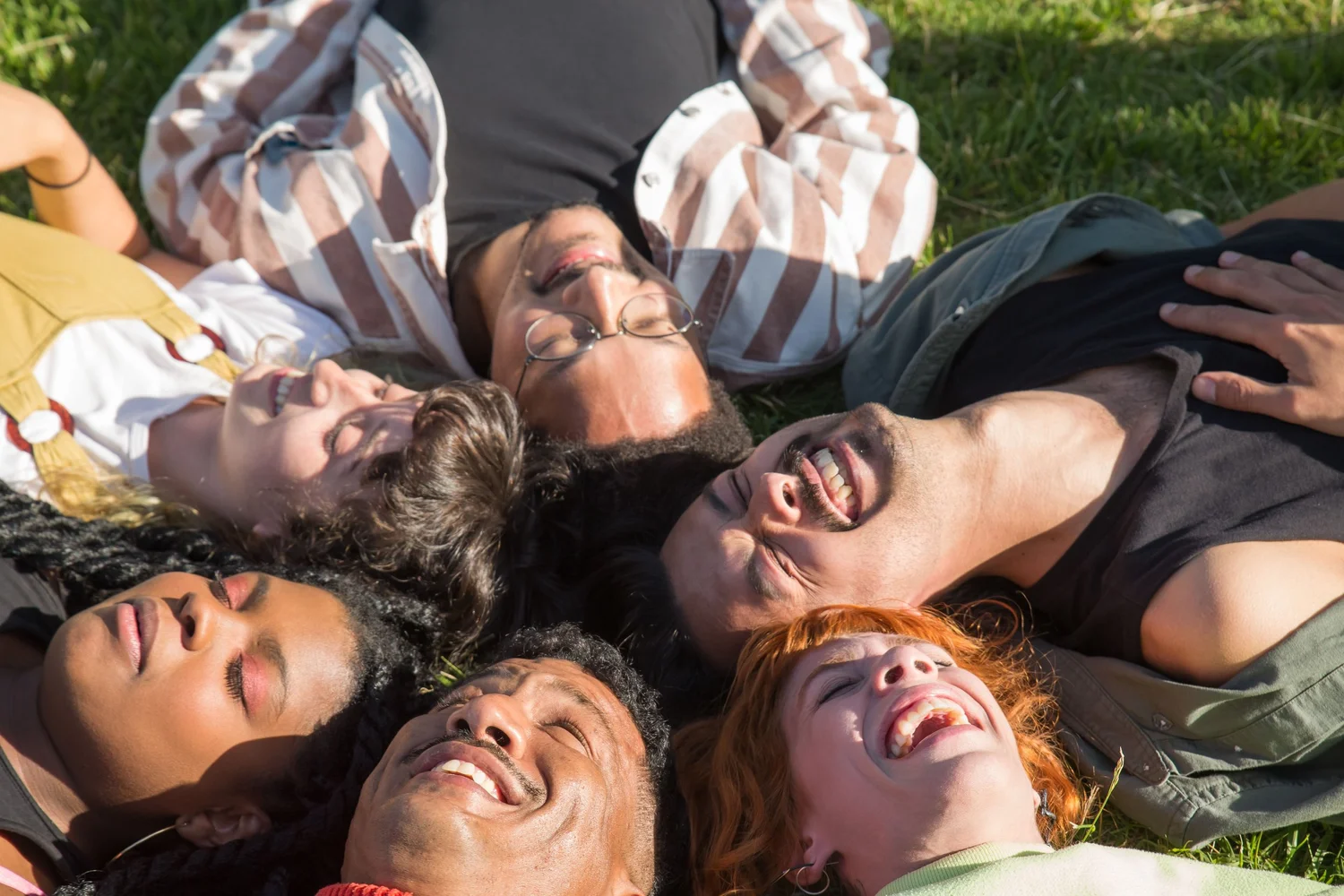 A group of people lying in a circle on the grass, smiling together.