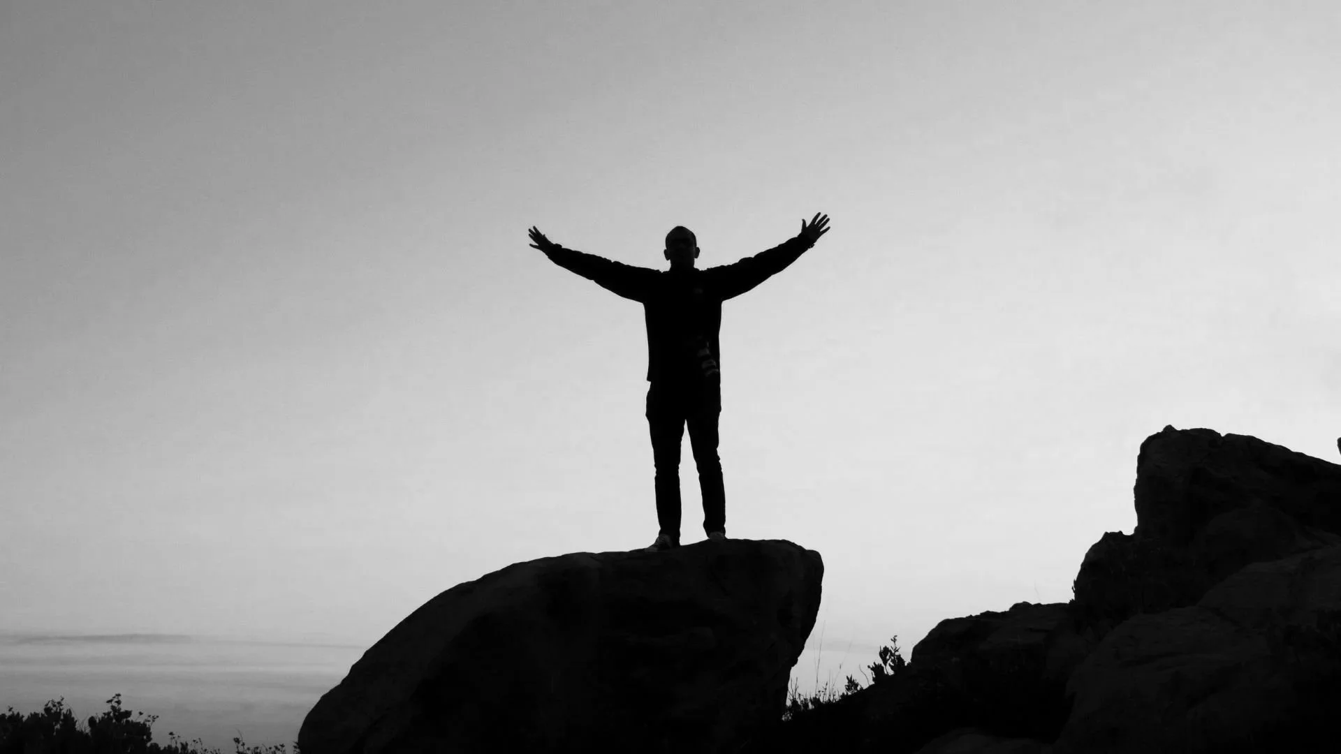 Silhouette of a person standing on a large rock with arms outstretched against the sky.