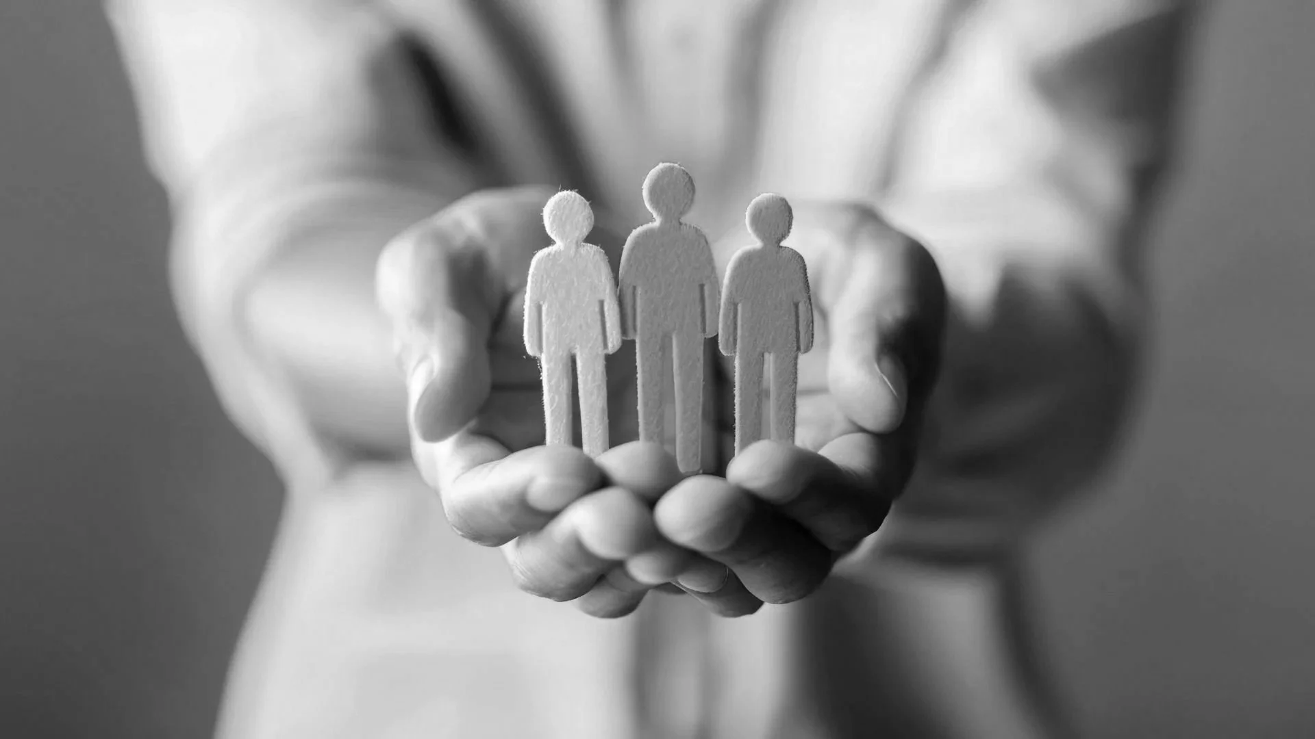 A person holding three paper cutout figures of people in black and white.