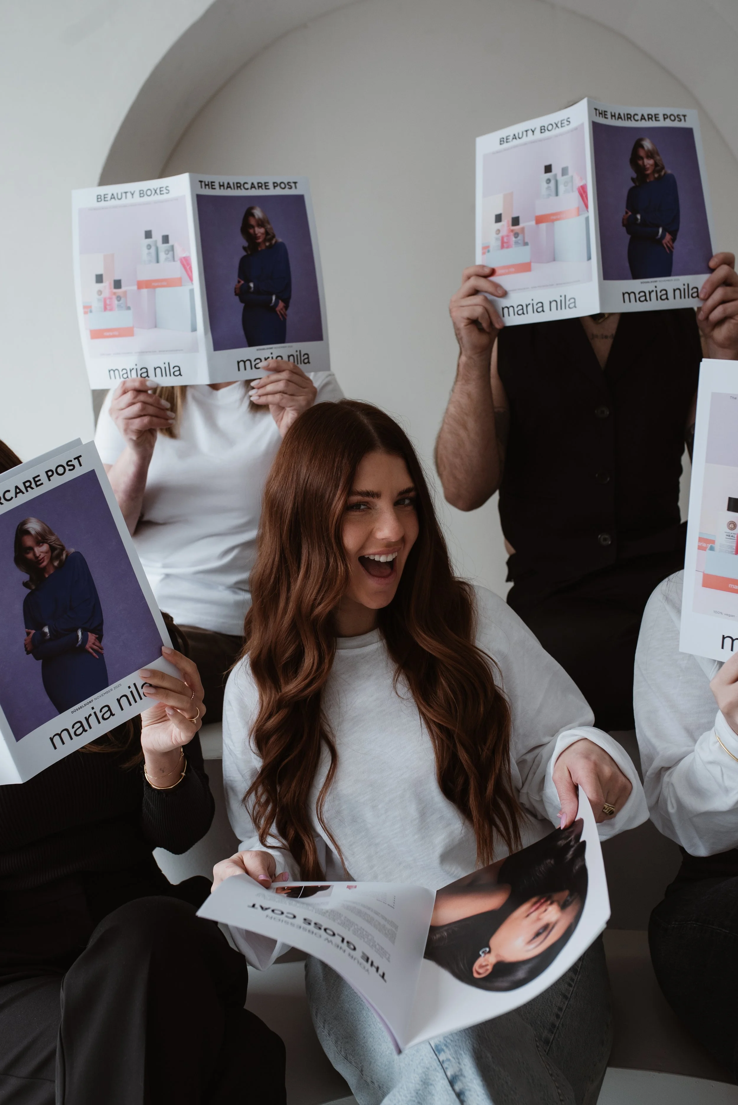 Menschen, die Magazine bei einem Gemeinschaftstreffen lesen, mit unterschiedlichen Hauttönen und Haarfarben, sitzend an einem weißen Ort.