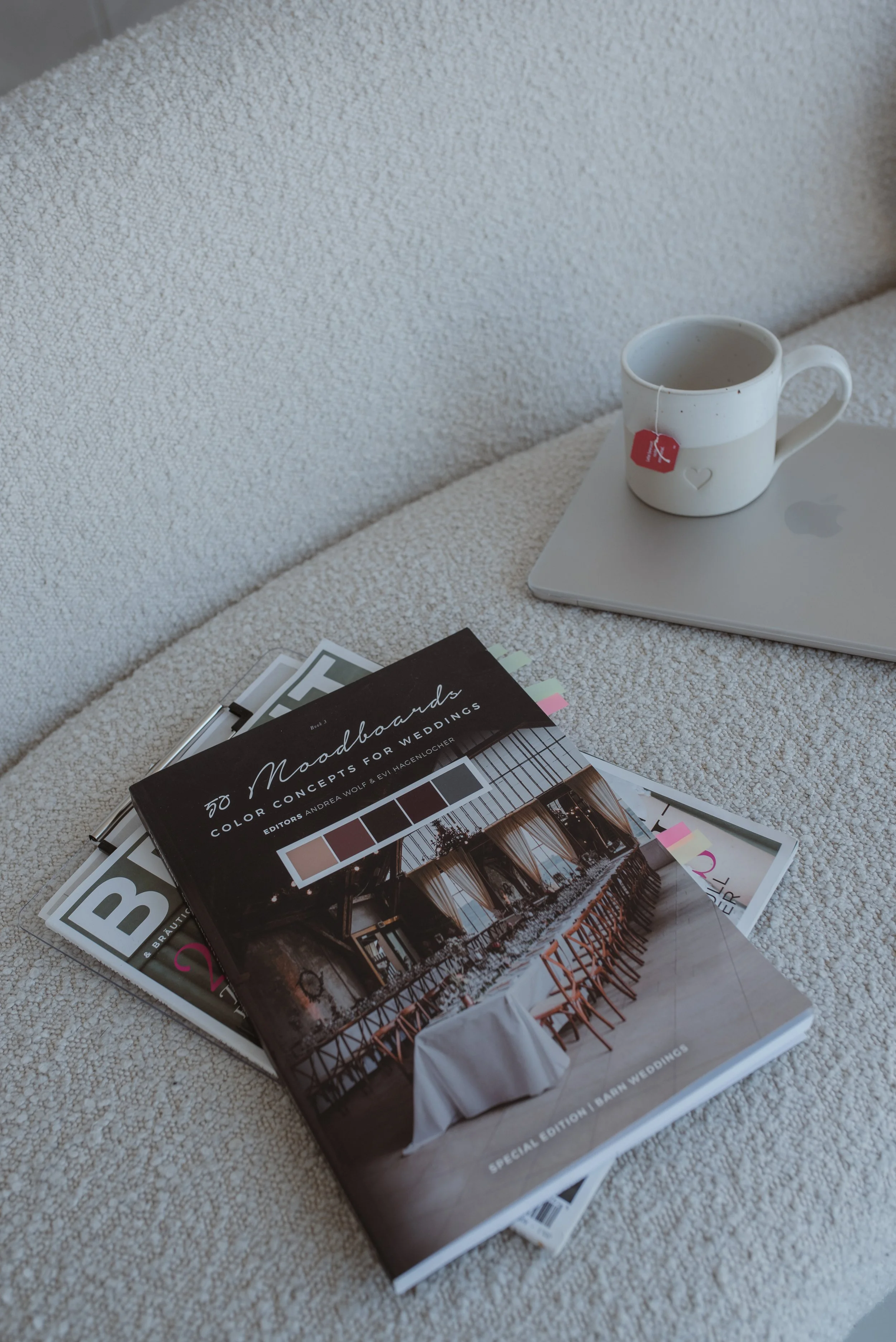 Auf einem Tisch liegen mehrere Magazine, ein Laptop, eine Kaffeetasse und an einem Magazin befestigte Farbfächer.