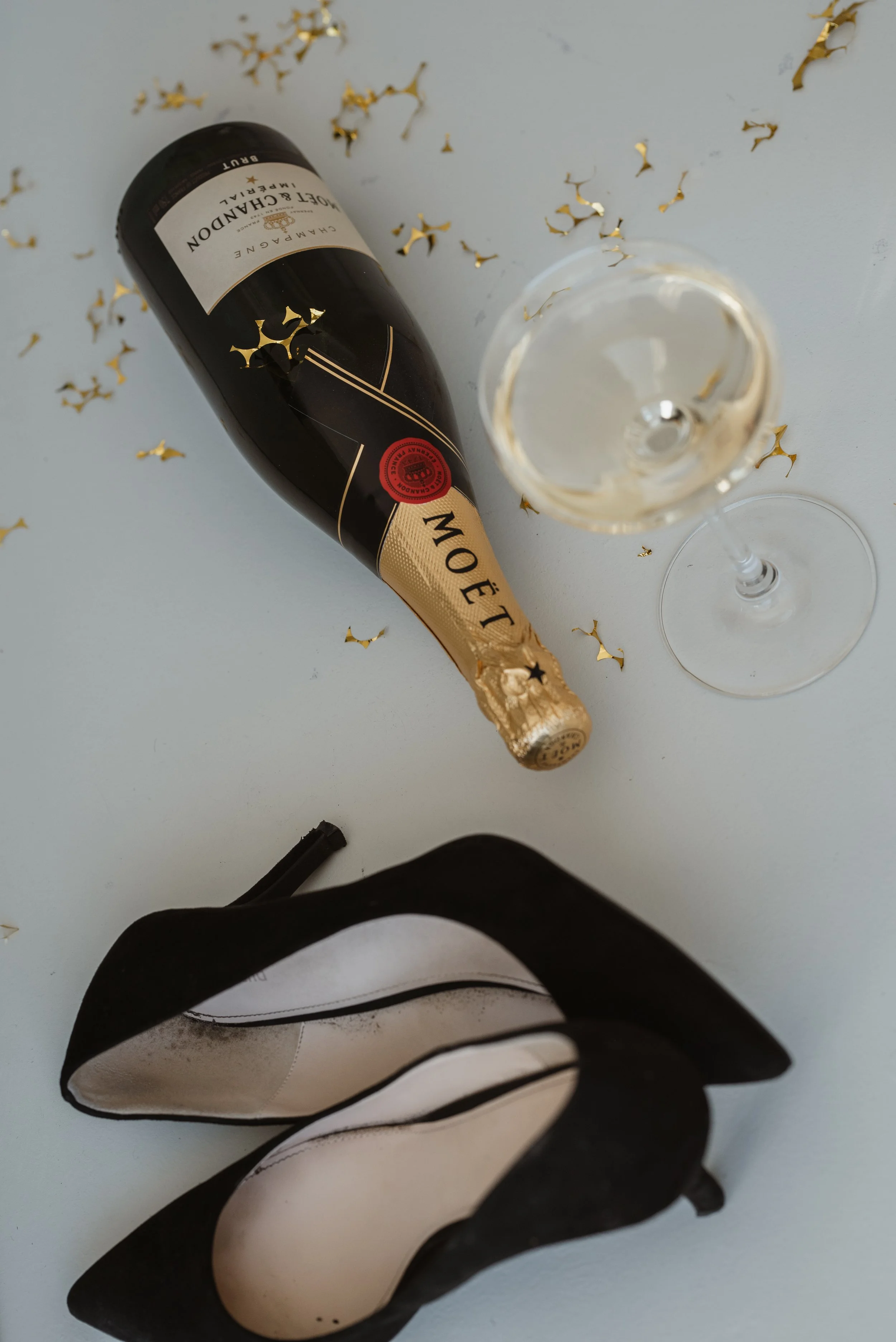 Sektflasche mit Goldfolienkrone, Sektglas mit Sekt, schwarze und weiße Geschenk- oder Einkaufstasche auf weißem Hintergrund mit Partydekoration, einschließlich goldfarbenem Konfetti.