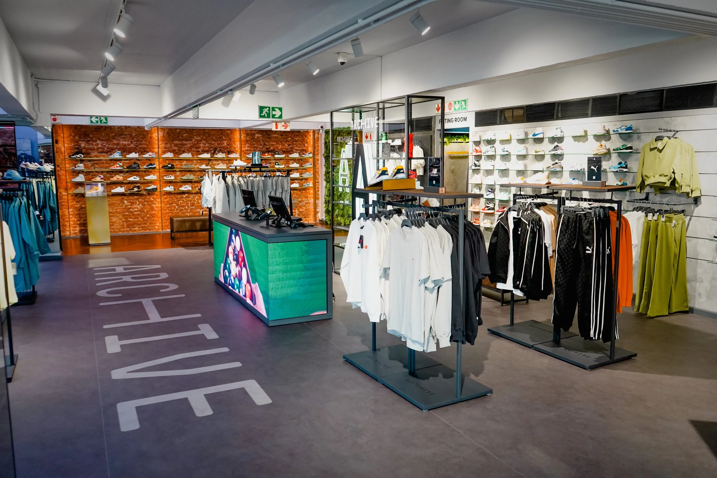 Interior of a retail store featuring sports shoes, clothing, and a digital display.