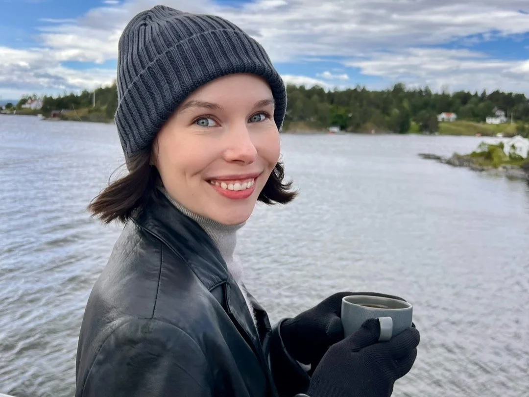 Woman on a fjord cruises holds a cup of coffee and smiles at the camera