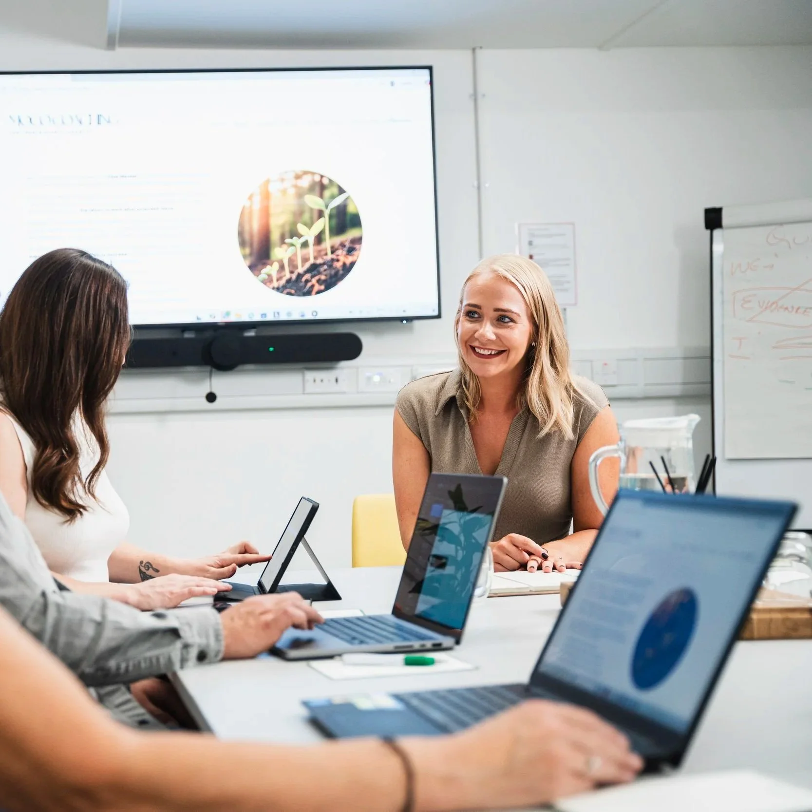 A dark workspace with green and black accents, featuring a desk with an open book, notebooks, and various decorative plants, containers, and a black desk lamp.