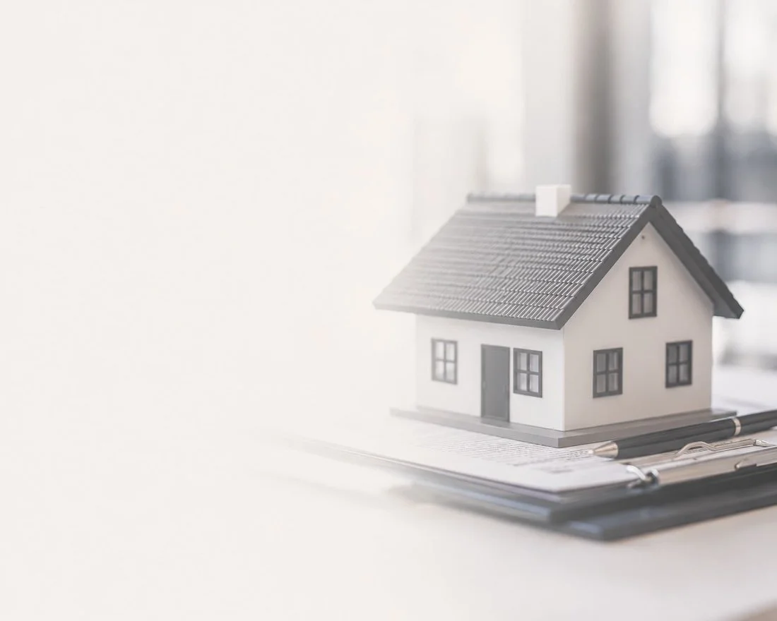 Miniature model of a house placed on a clipboard with a pen in front.