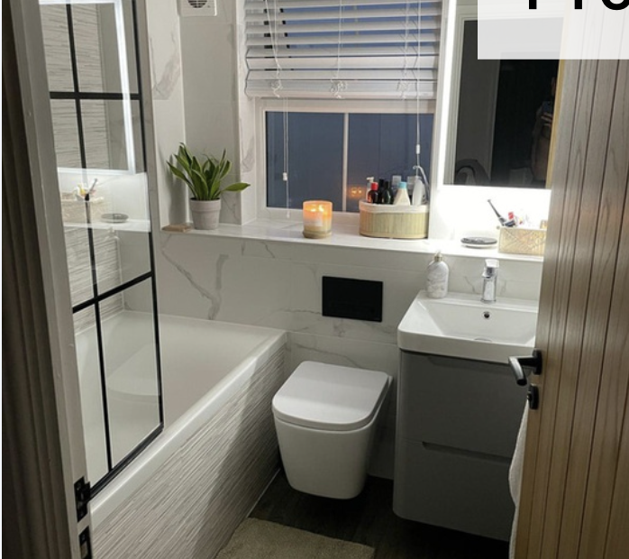 Small modern bathroom with a bathtub, a window with blinds, a potted plant, a candle, a countertop with toiletries, a toilet, and a sink with a mirror.