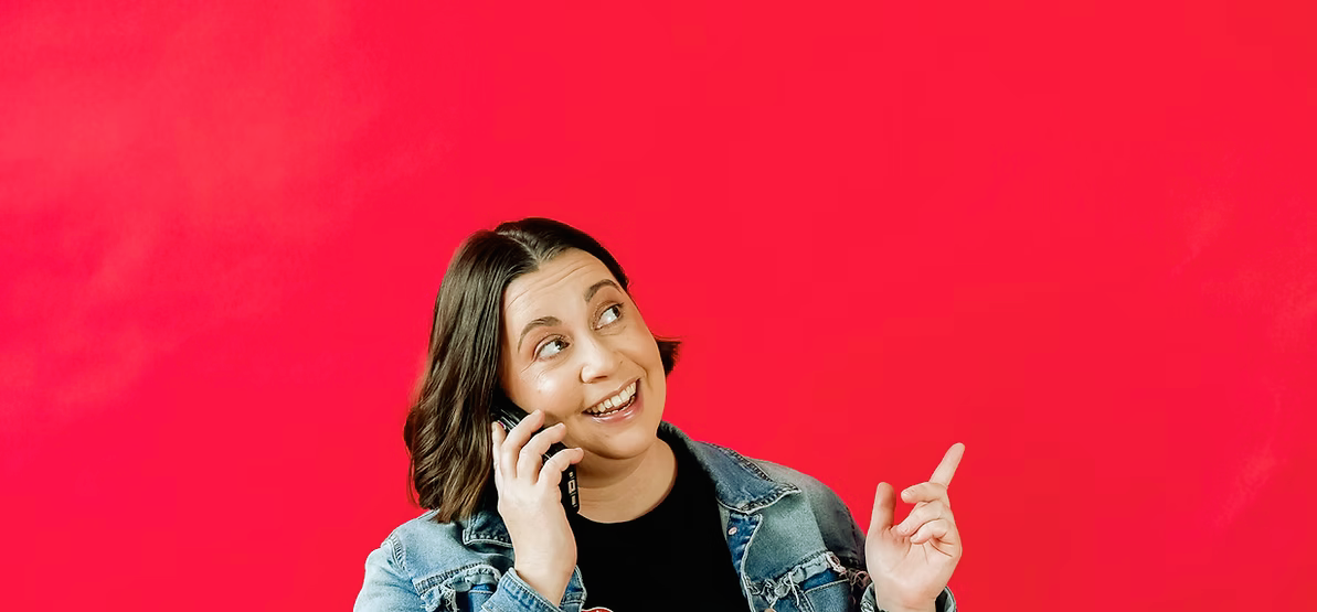 Young woman talking on a cell phone while pointing upward, against a red background.