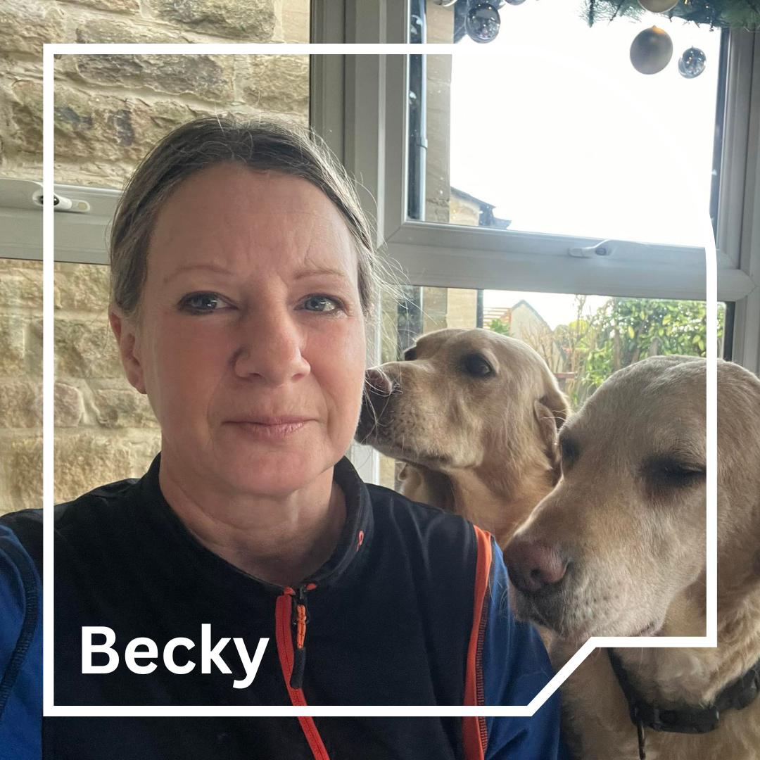 Woman looking at the camera, with two yellow labradors sat beside her