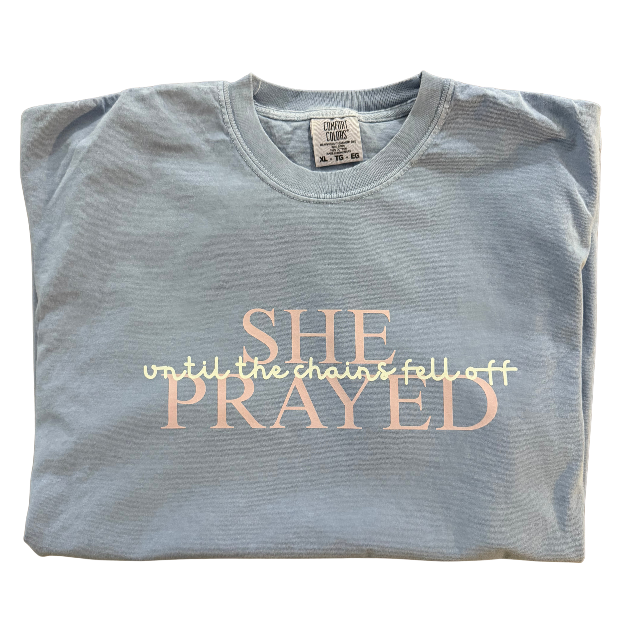 Light blue T-shirt with pink and white text that says 'SHE PRAYED until the chains fell off' on a black background.