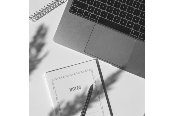 Laptop, Notizbuch, Stift und Schatten auf einem Schreibtisch