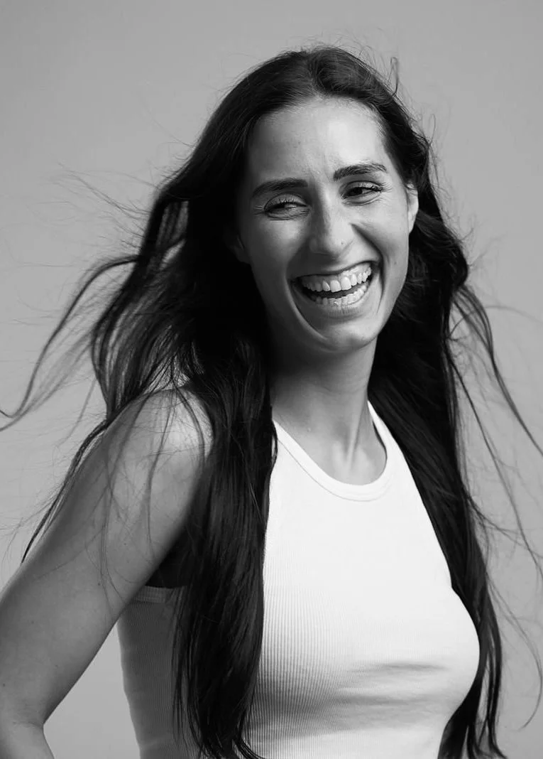 Lachende junge Frau mit langen dunklen Haaren vor hellem Hintergrund, schwarz-weiß