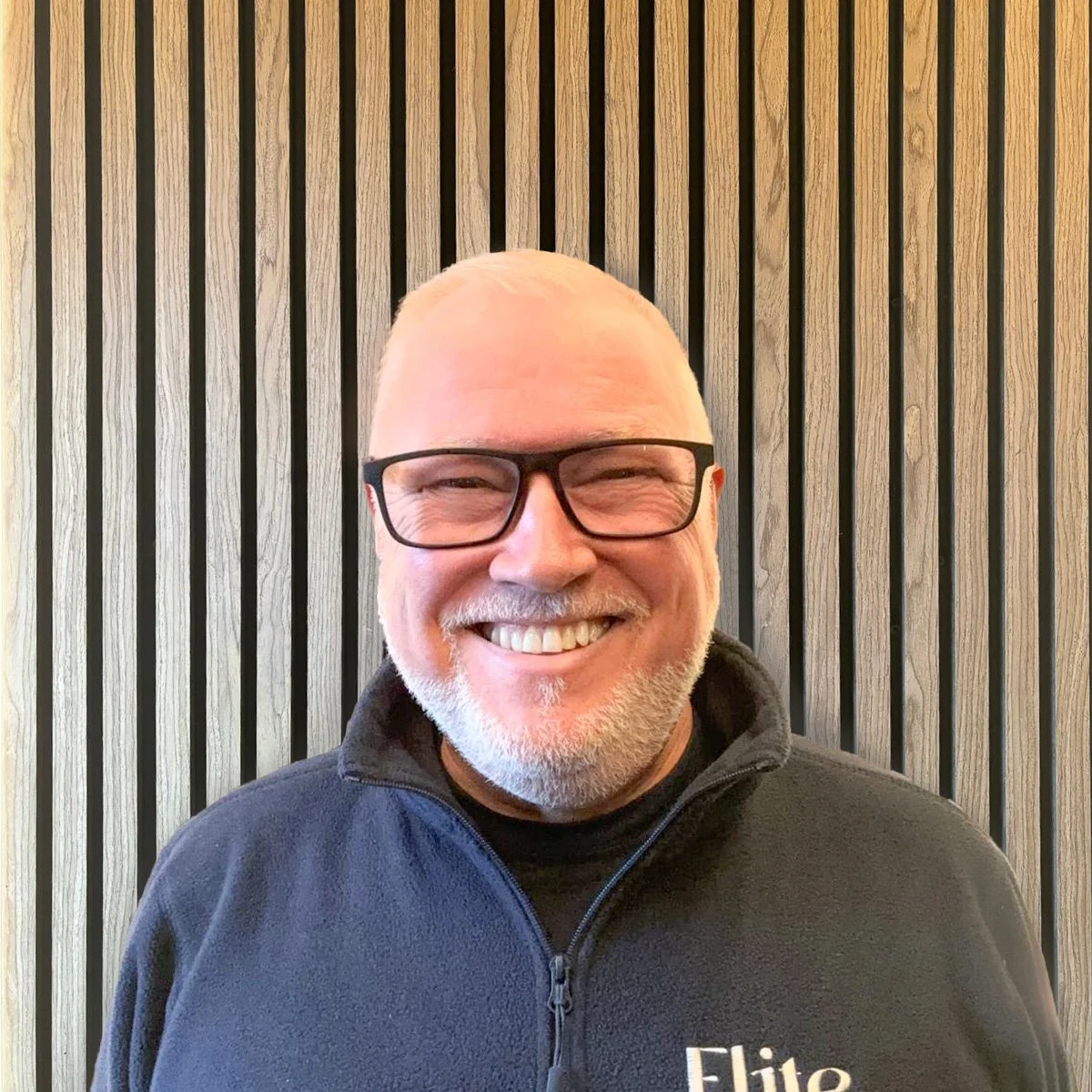 Smiling middle-aged man with glasses and a beard sitting at a restaurant table.