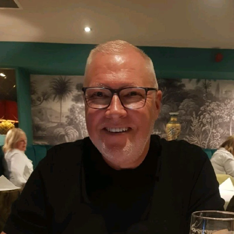 Smiling middle-aged man with glasses and a beard sitting at a restaurant table.