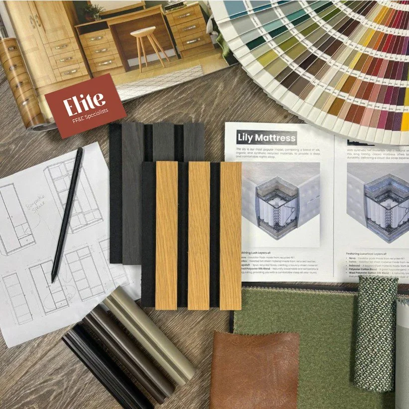 Interior design samples and materials on a wooden table, including color swatches, wood planks, fabric swatches, a chair sketch, and a Lily Mattress brochure.