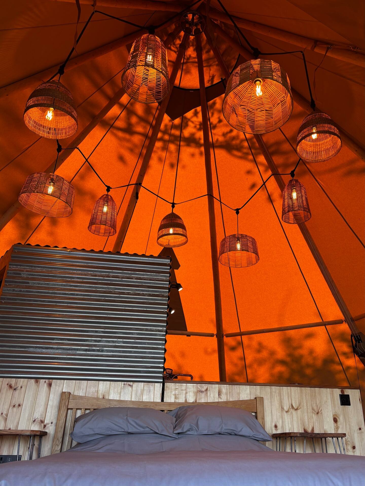 Inside a tent with hanging woven lamps and a bed with gray sheets and pillows.