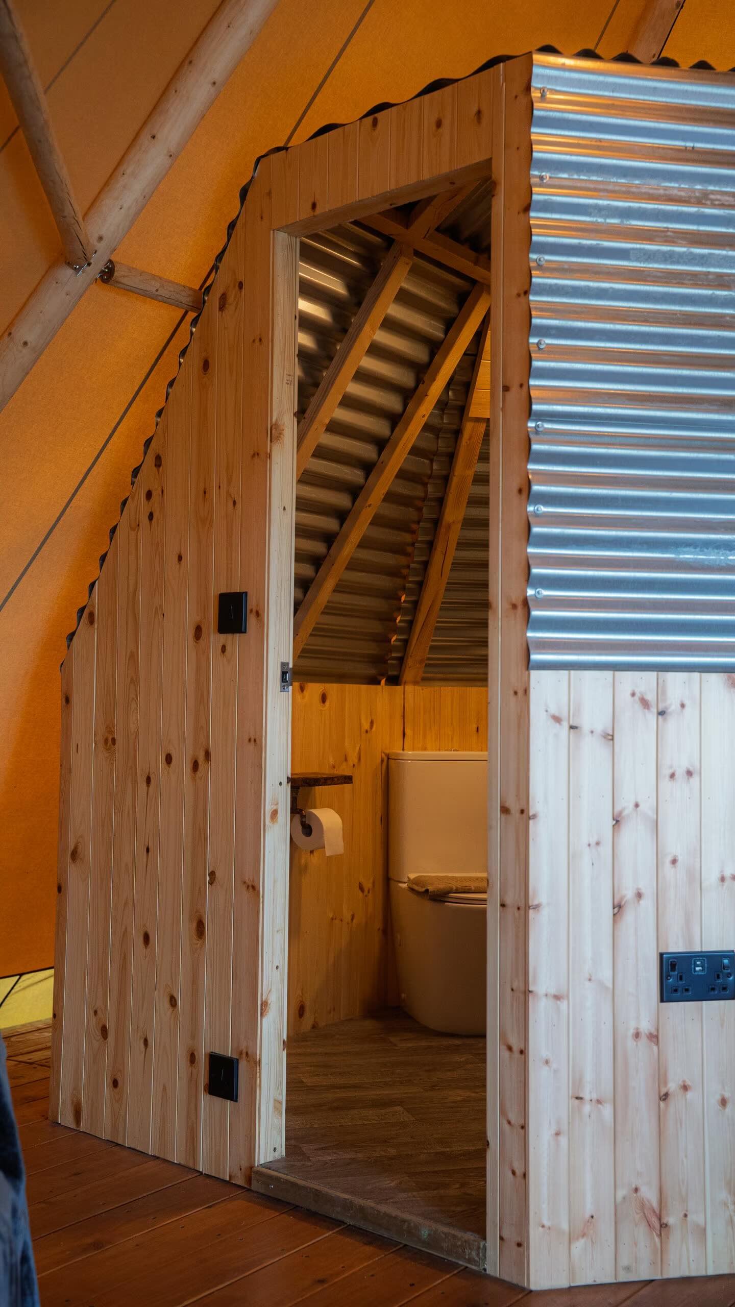 Wooden bathroom stall with a toilet inside, some paper towels, and wood-paneled walls.