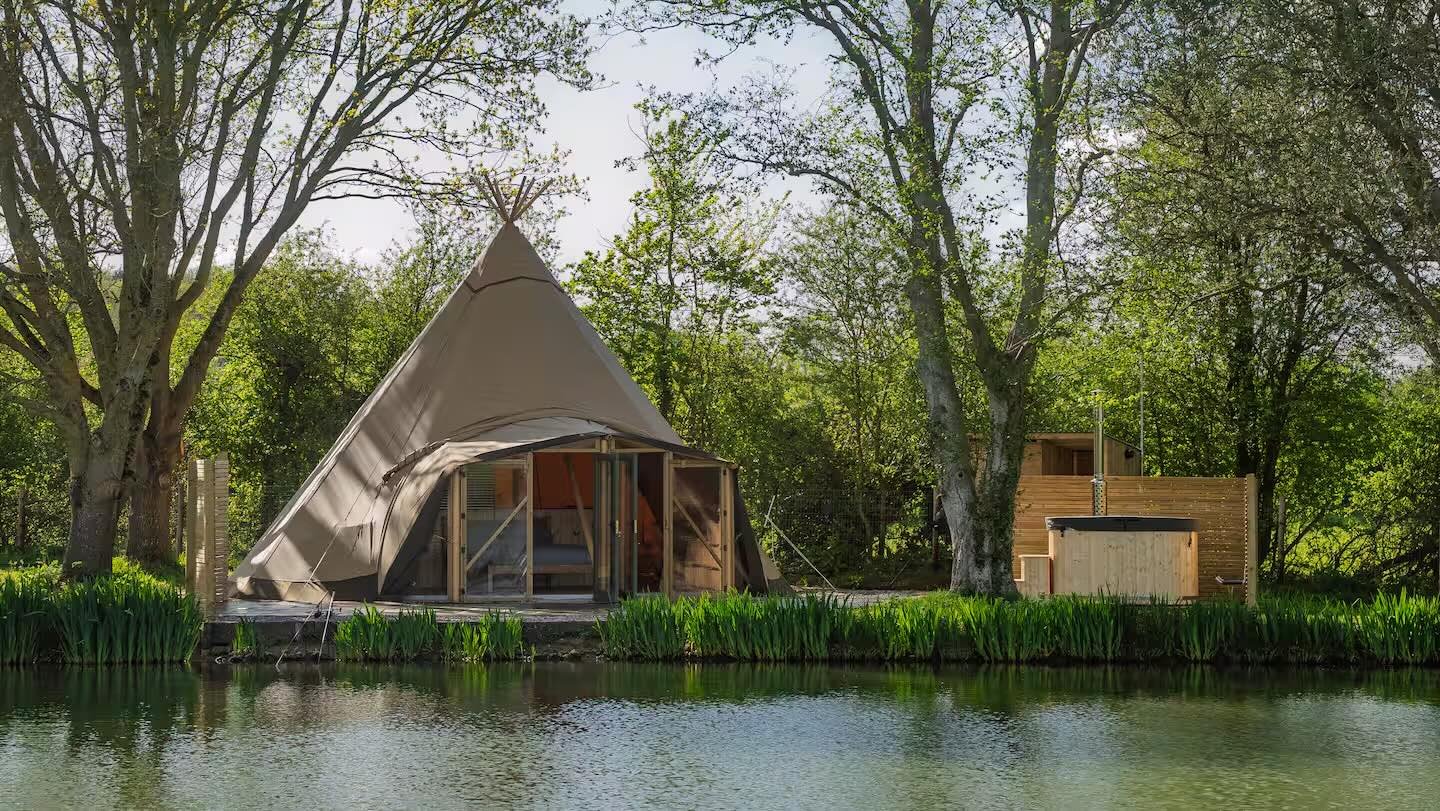 A tent by a riverside surrounded by trees with green foliage.