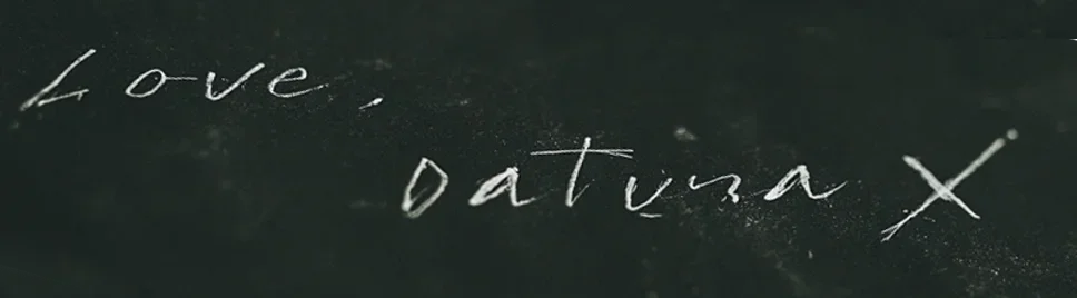 Close-up of handwritten text on a dark surface, reading 'Love, Datura X'.