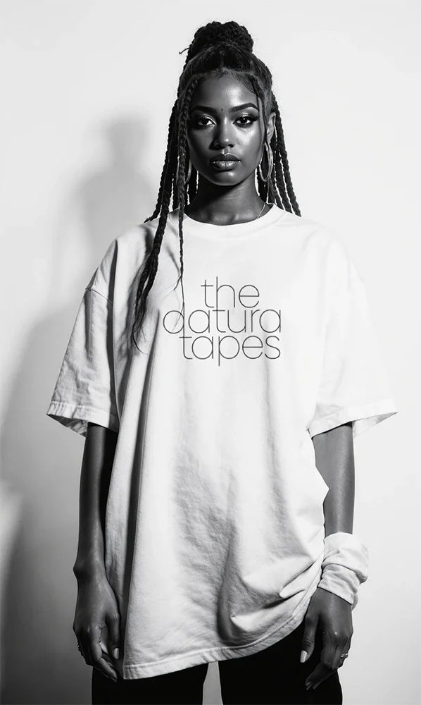 Black woman with braided hair and hoop earrings wearing an oversized T-shirt with "the natura tapes" text, standing against a plain background.