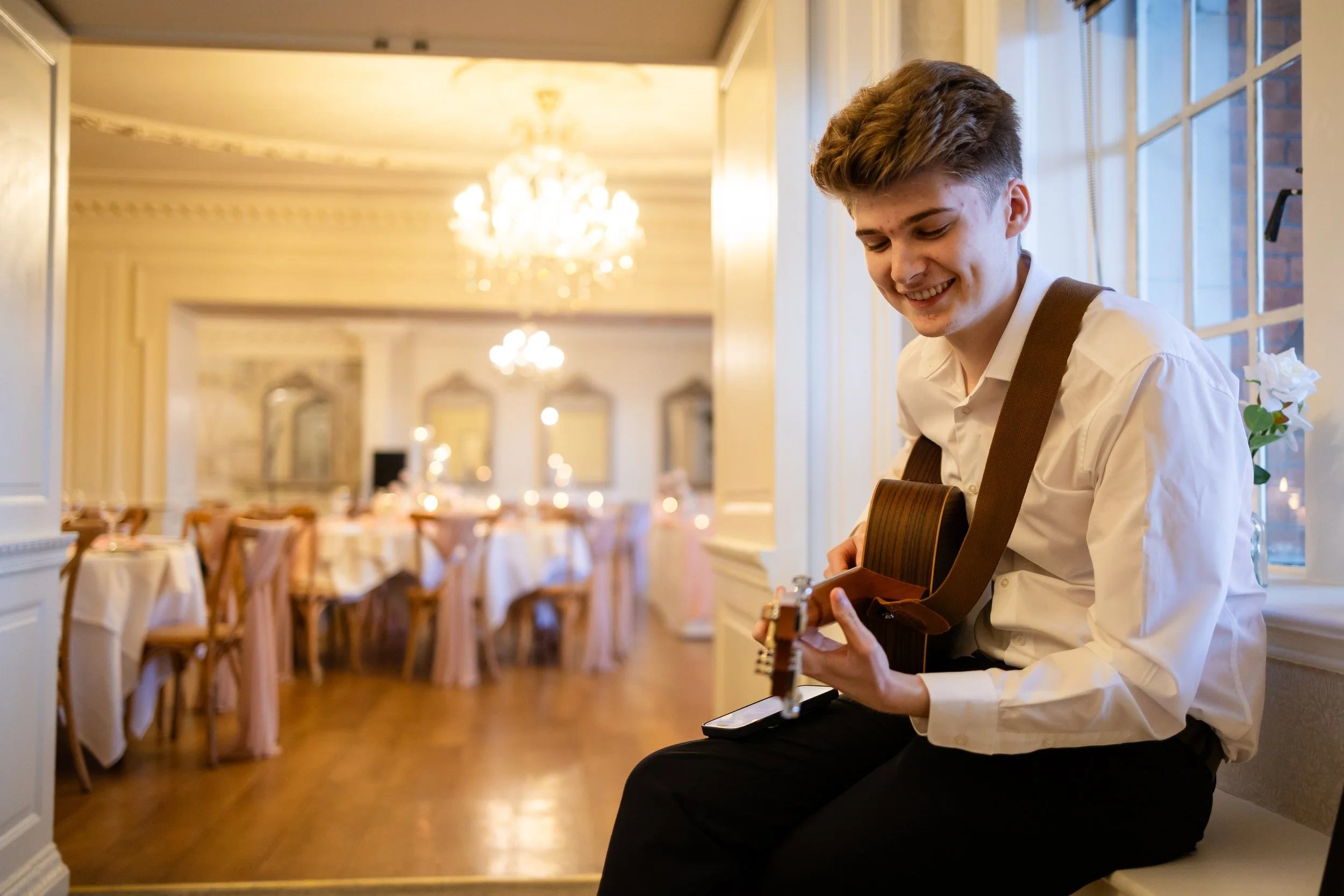 Oscar Flanagan sitting on a bench at Eaves Hall playing his acoustic guitar