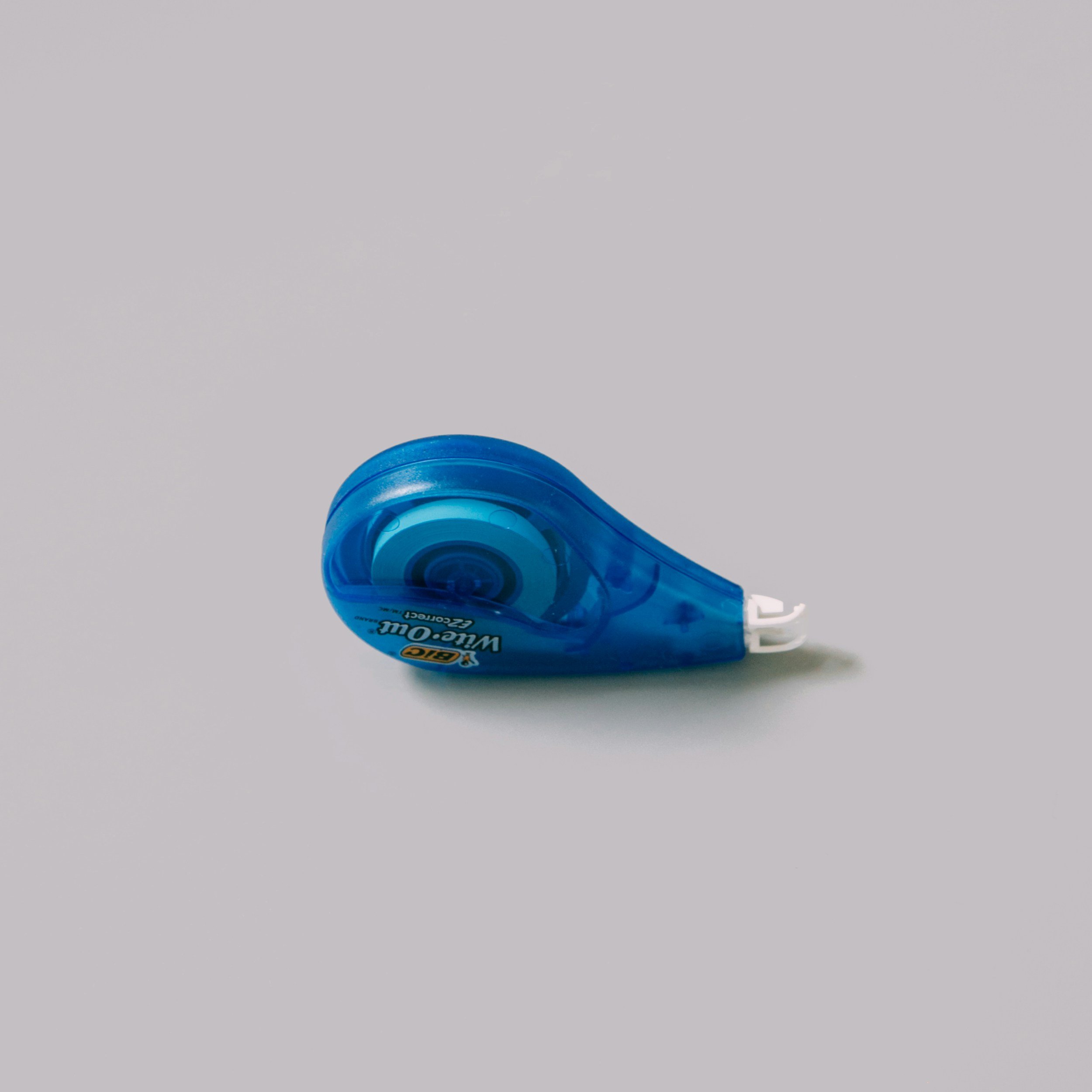 A blue correction tape dispenser placed on a light gray surface.