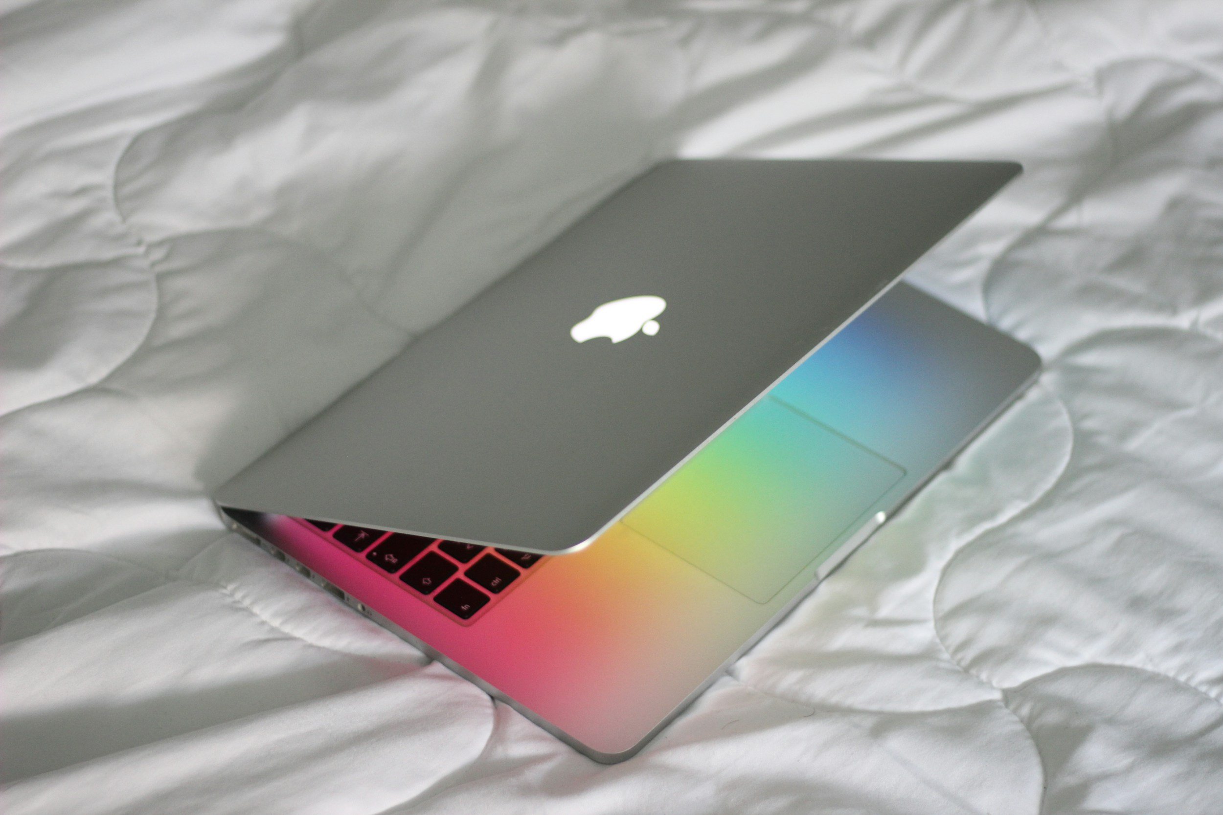 A silver MacBook laptop with an illuminated apple logo on the lid, partially opened, resting on a white quilted surface.