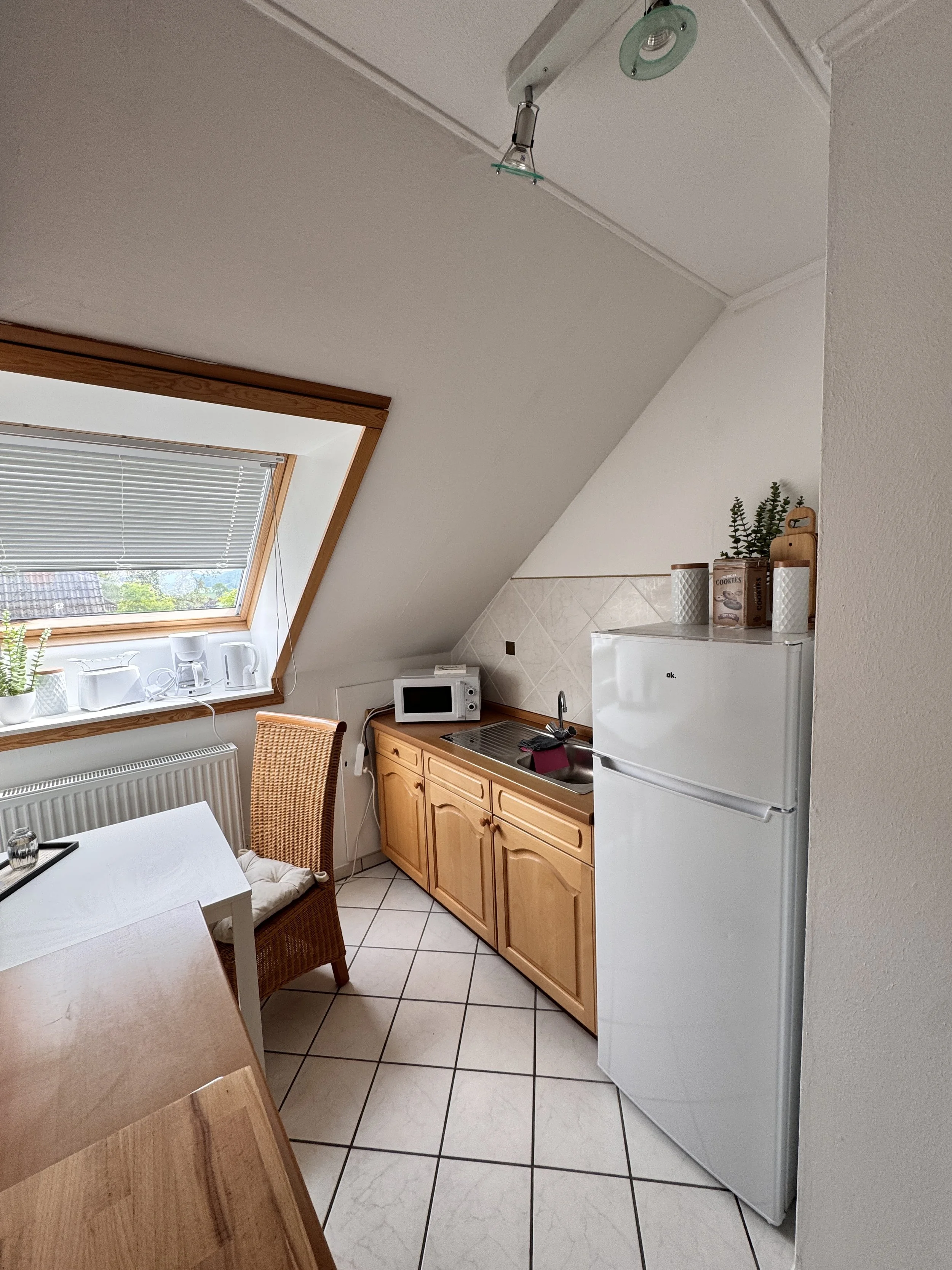 Küche mit kleiner Küchenzeile, Mikrowelle, Kühlschrank, Fenster unter Schräge mit Vorhängen