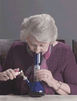 An elderly woman uses a blue medical inhaler and a nebulizer to breathe into a snorkel-like device.