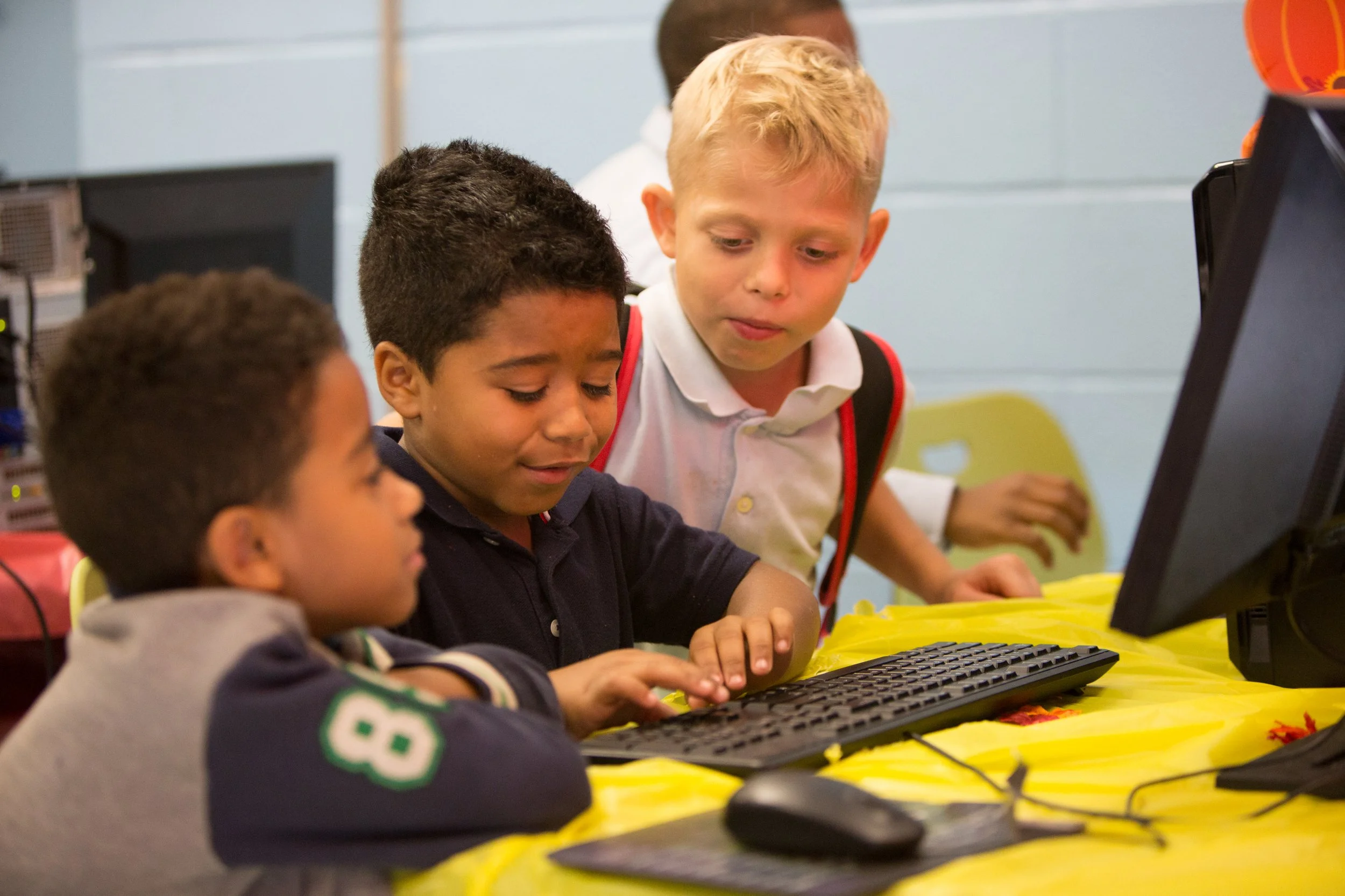 Three young boys gathered around a computer, working together in a classroom setting.