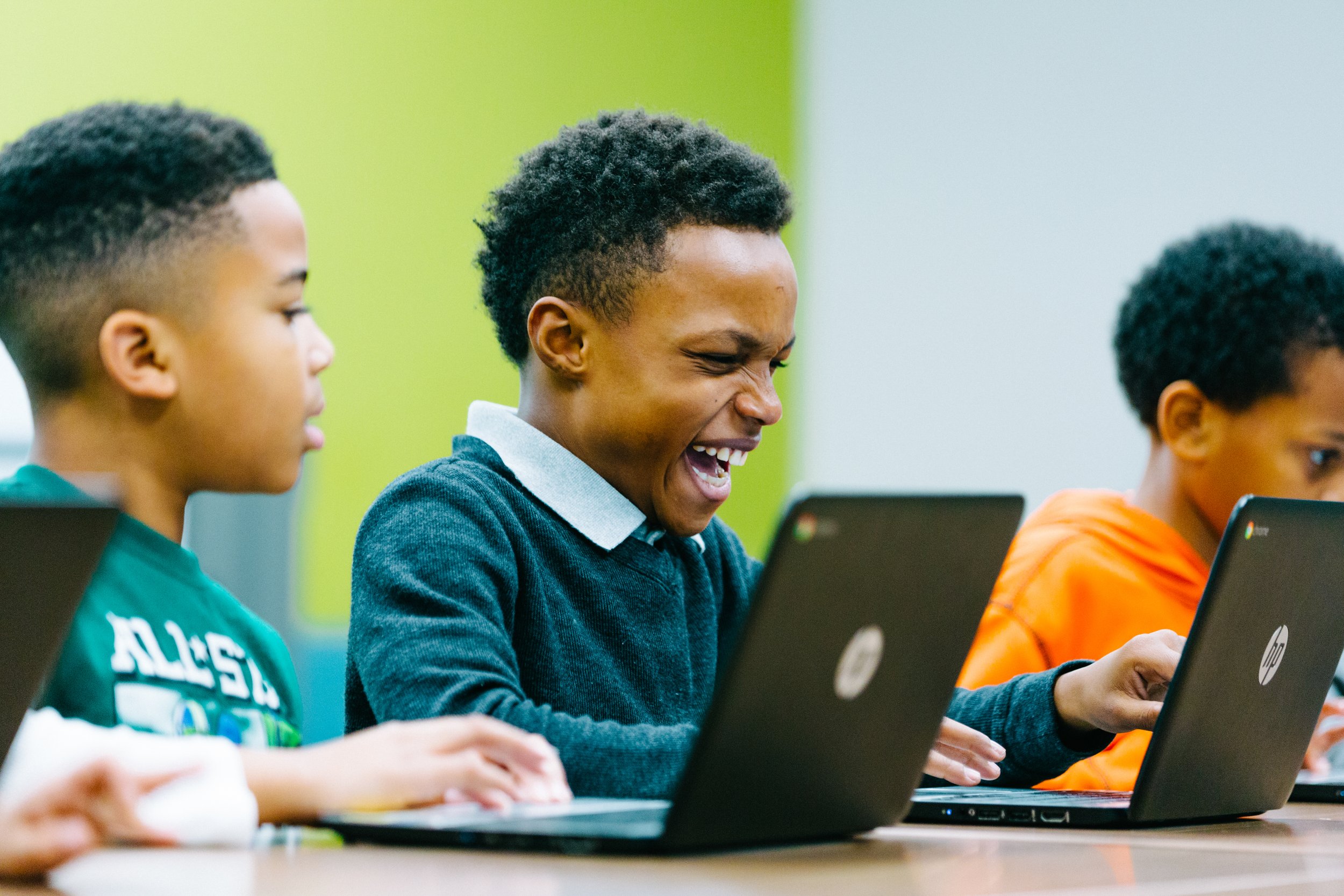 Children using laptops in a classroom, with one girl laughing.