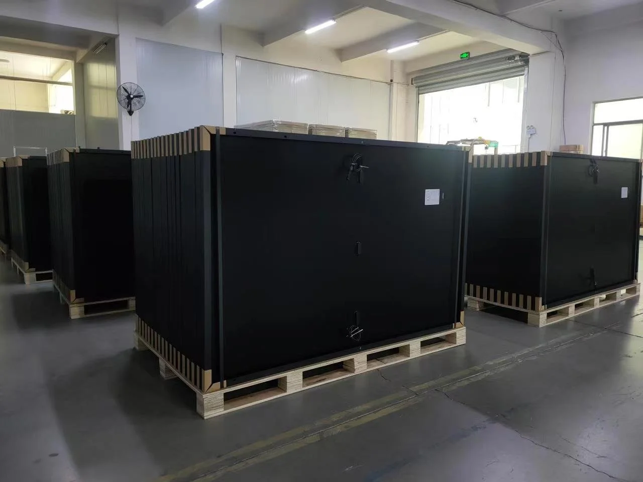 Large black crates on wooden pallets inside a warehouse.