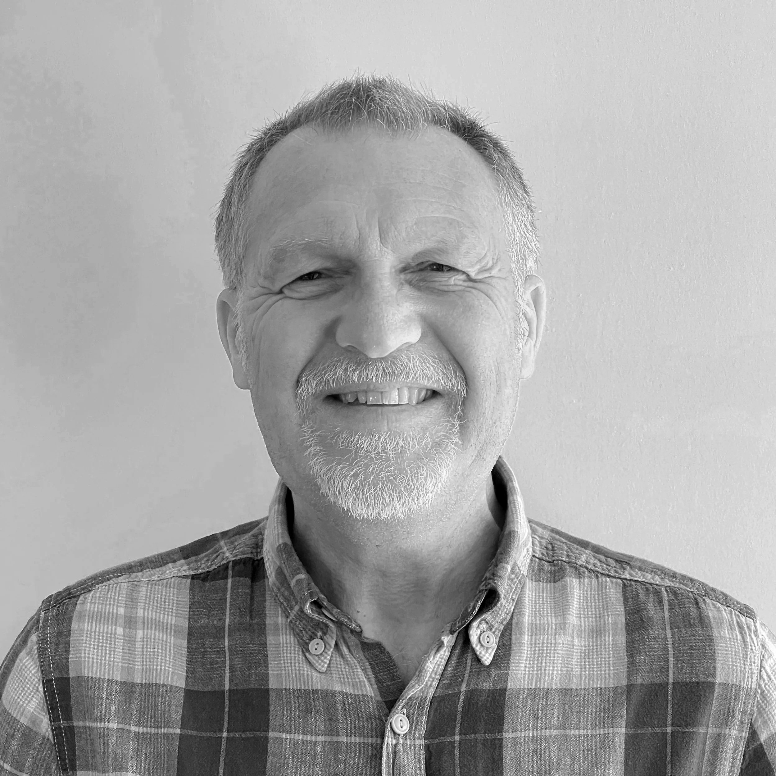 Black and white headshot of a smiling middle-aged man with short hair, a beard, and wearing a striped shirt.