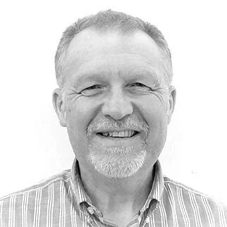 Black and white headshot of a smiling middle-aged man with short hair, a beard, and a collared shirt.