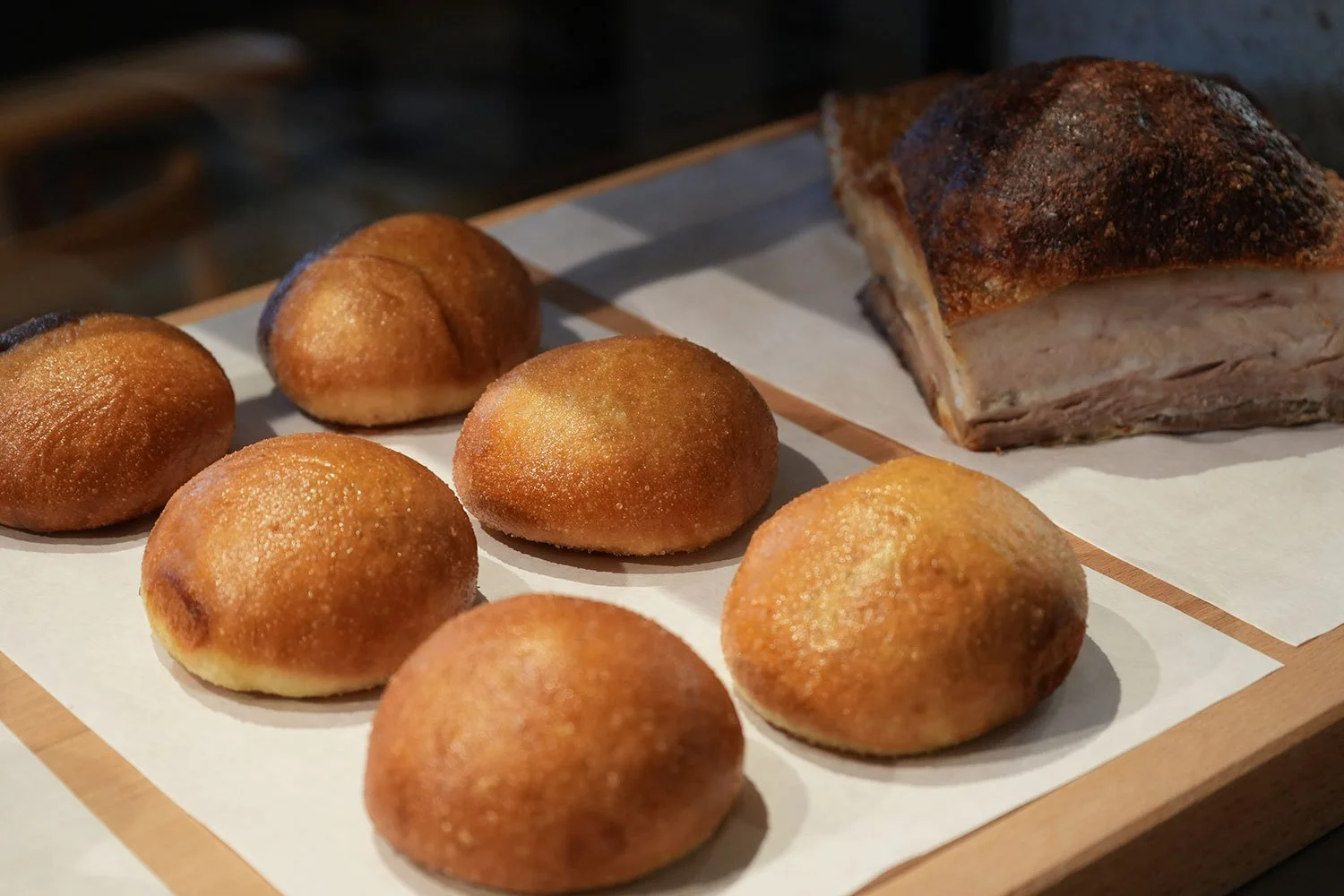 Fried dough balls and a large piece of roasted pork on a wooden tray with paper lining.