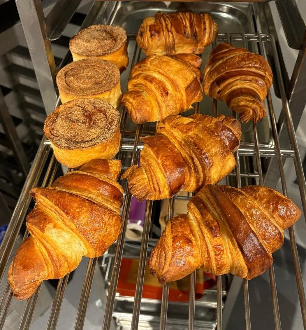 An assortment of croissants and cinnamon rolls cooling on a wire rack.