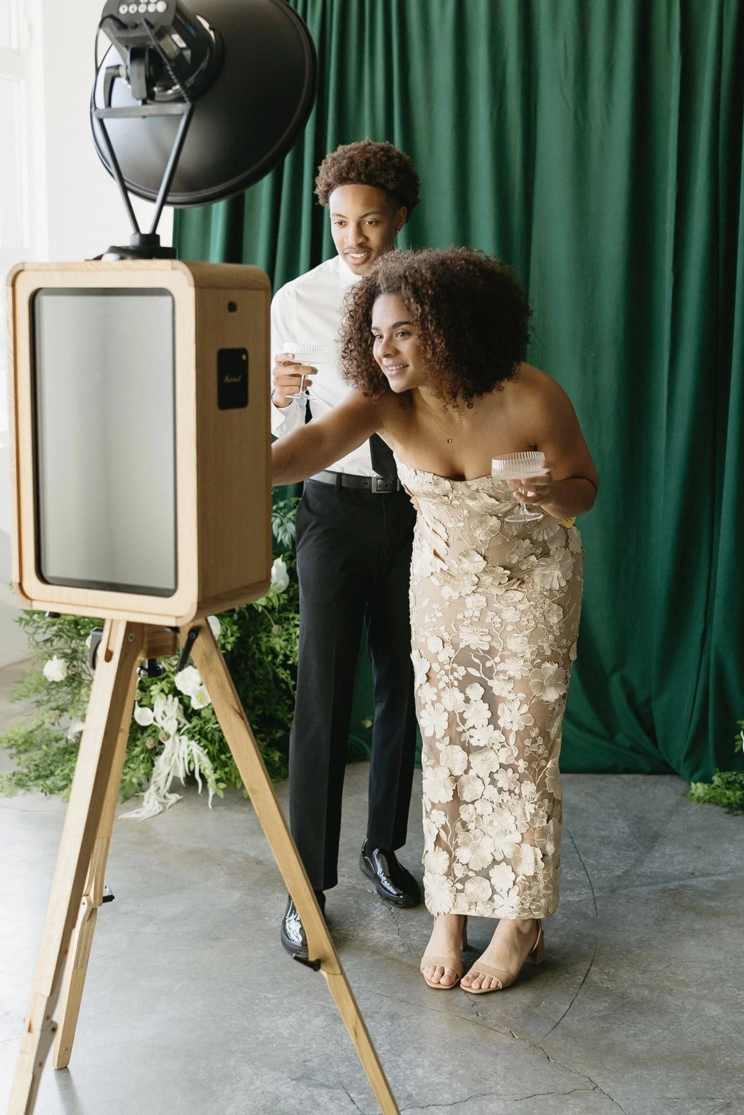 Couple posing together at a luxury photo booth rental with a styled green backdrop at a private event.