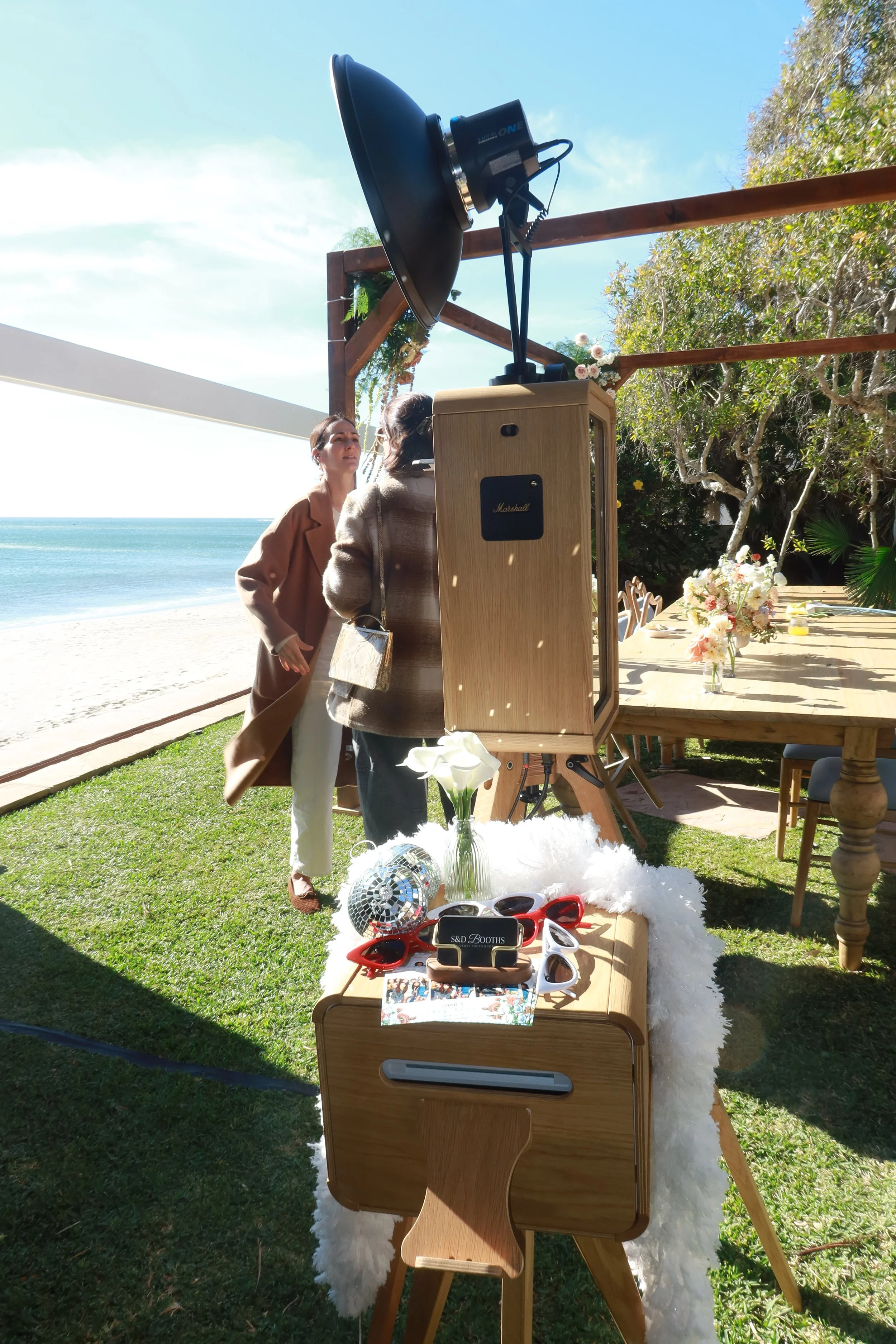 Outdoor luxury photo booth setup at a beachside event with custom props and professional lighting.