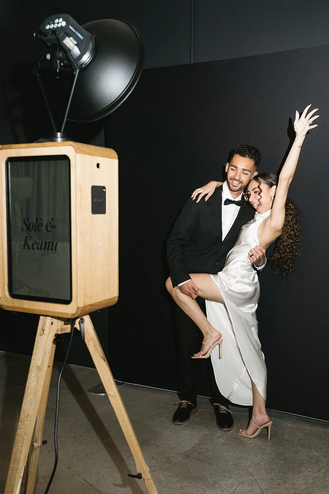 Wedding couple posing at a luxury photo booth rental featuring a handcrafted wooden photo booth.