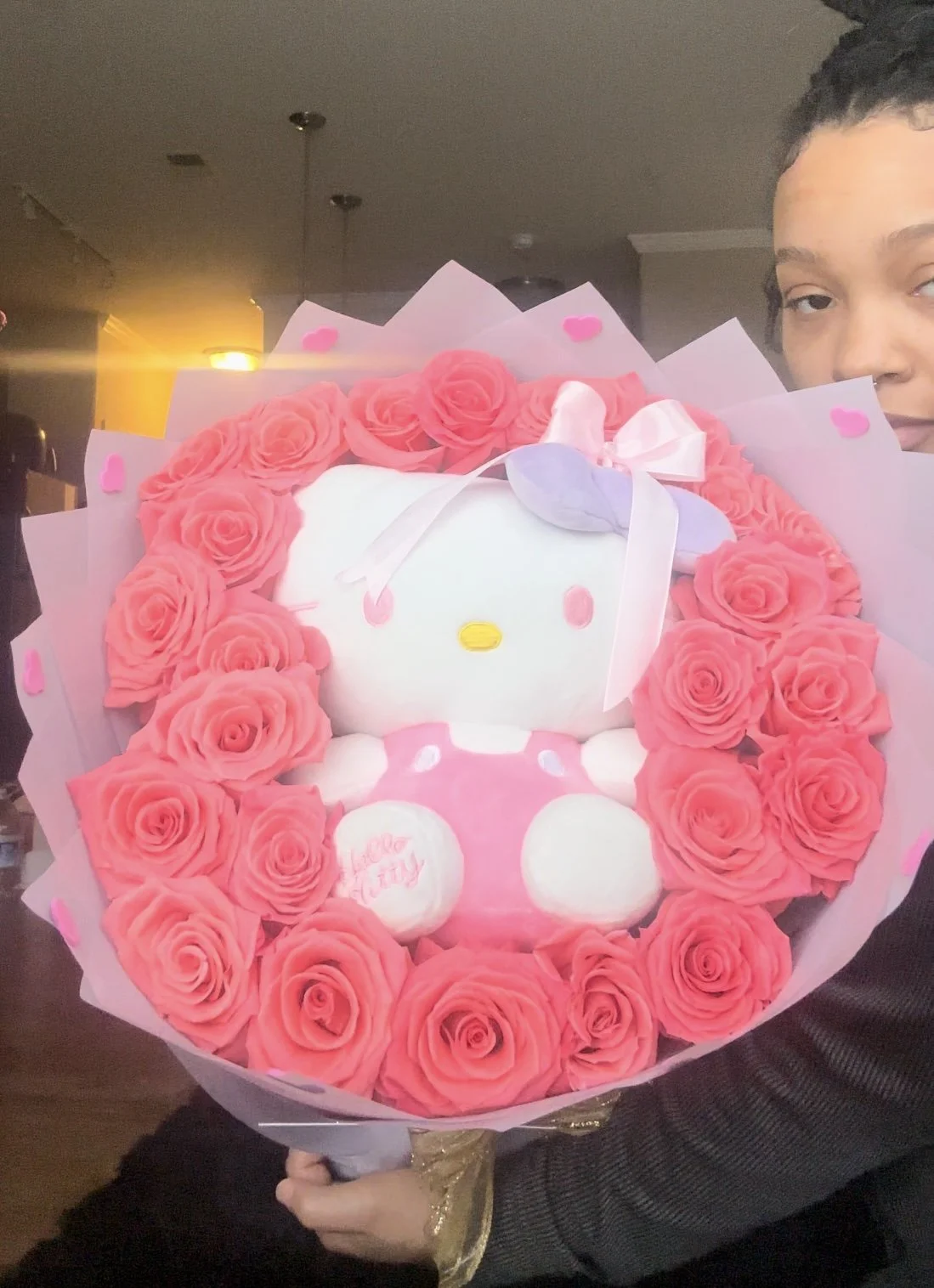 Person holding a bouquet with a Hello Kitty plush toy surrounded by pink roses and pink paper decorations.
